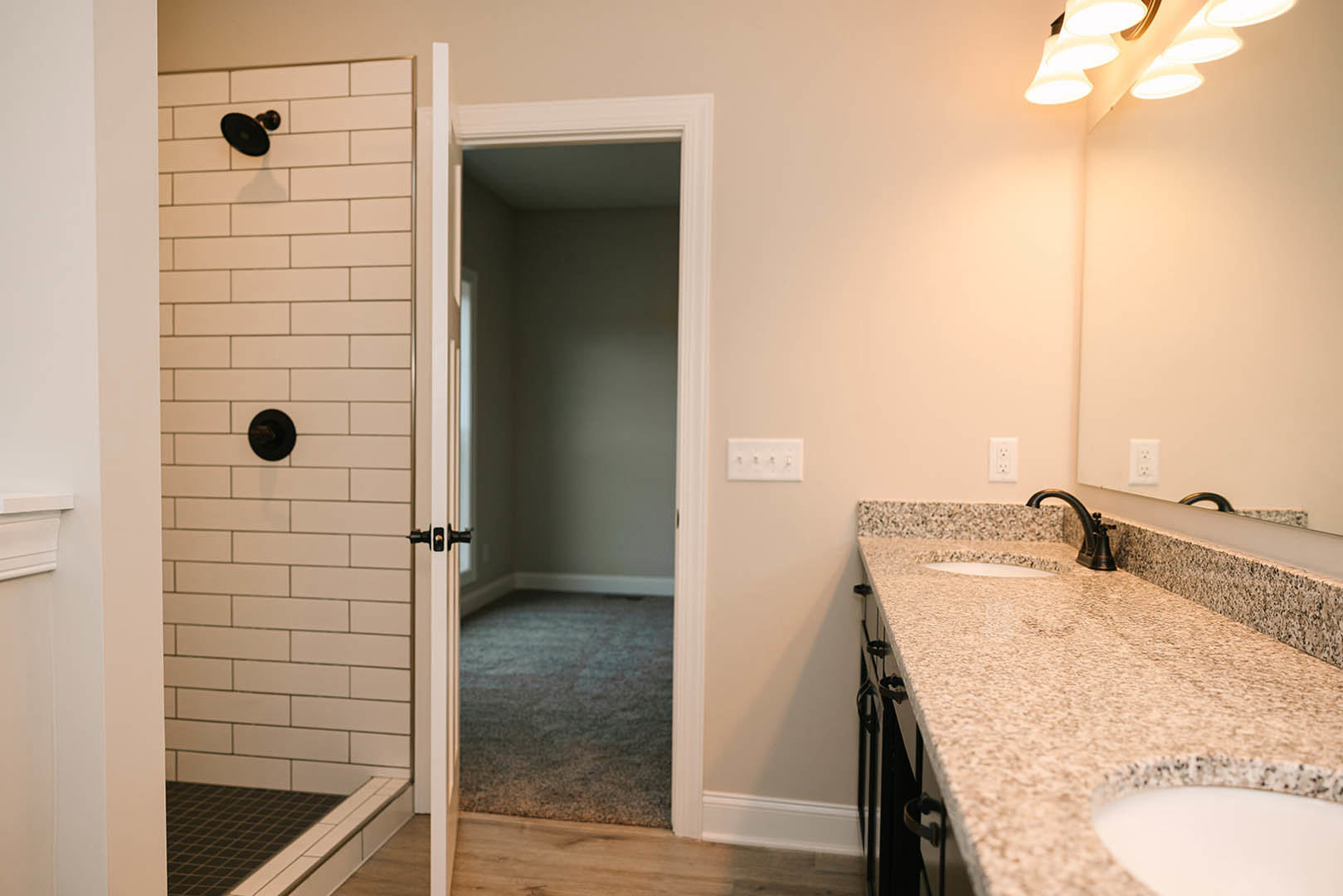 Modern bathroom featuring a walk-in shower with white subway tile walls, floating vanity with stone countertop, round mirror above sink, matte black fixtures, and light gray tile