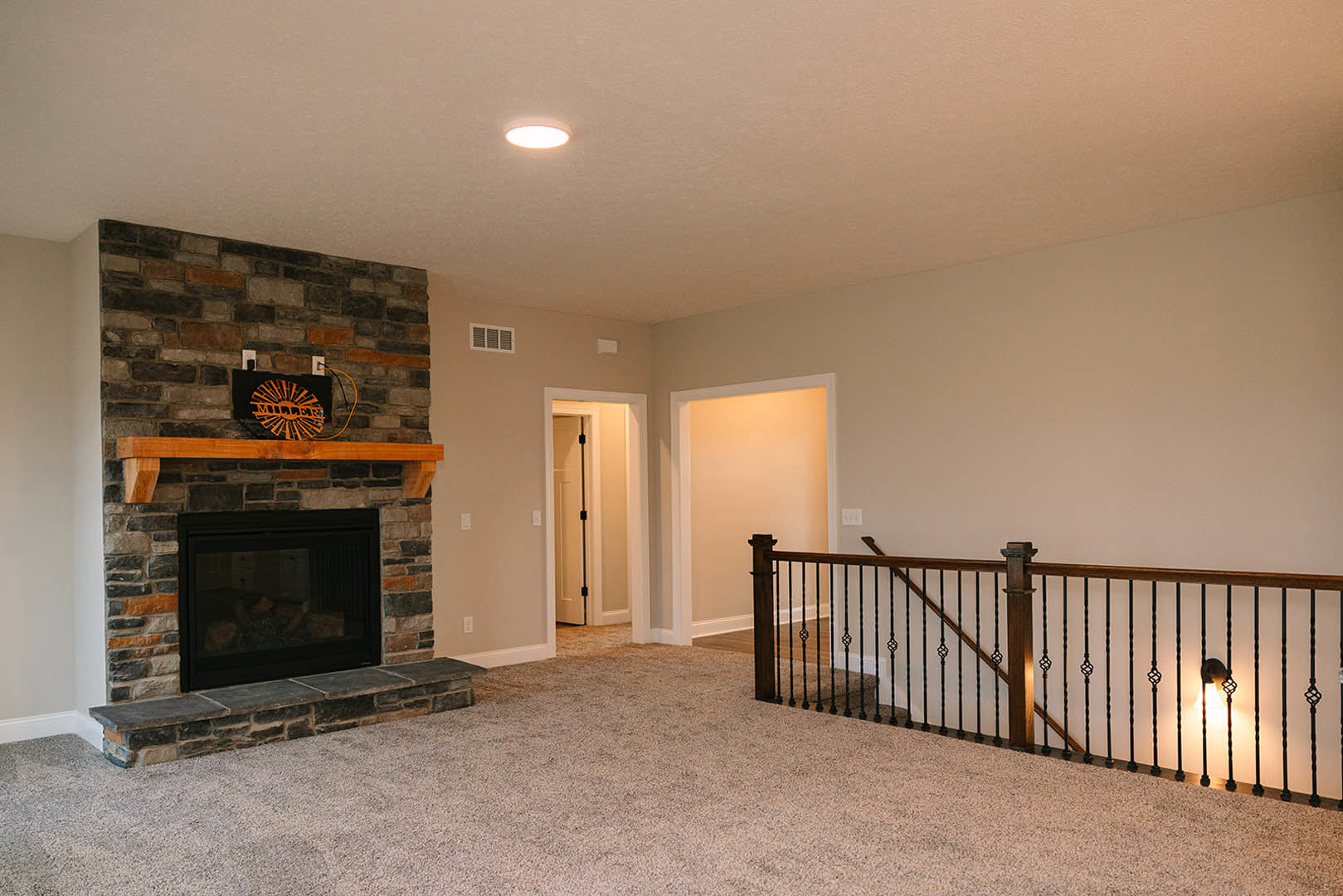 Living room featuring a glass-door fireplace, white plaster walls, black metal stair railing, wood flooring, and a lamp in the hallway