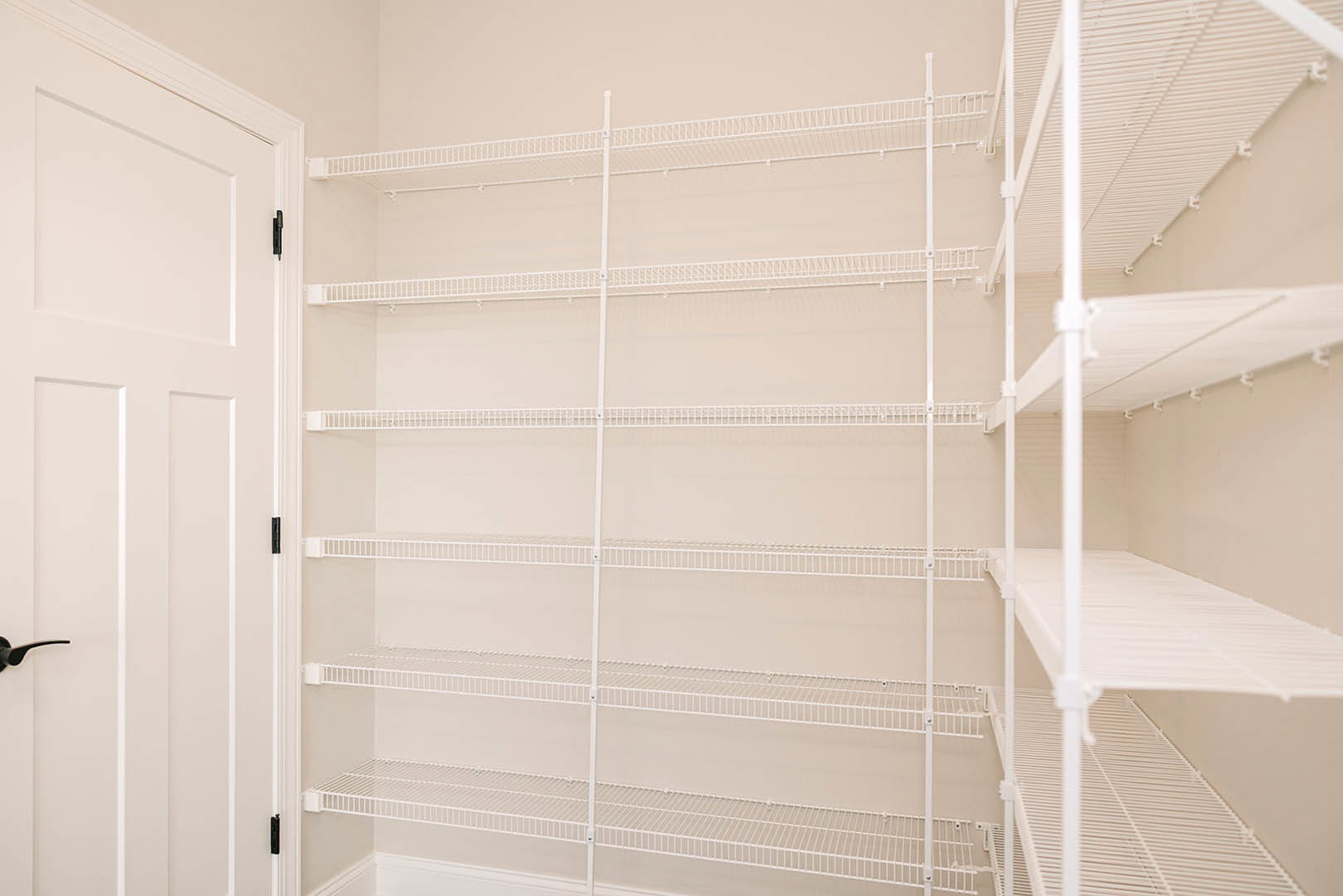 White built-in shelving unit against a light-colored wall, featuring neatly stacked white sheets and adjacent to a white door, with ceiling detail visible above.