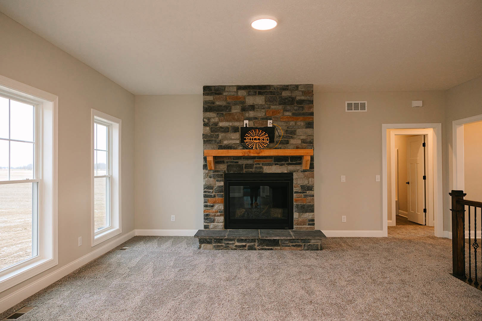Brick fireplace with glass doors reflecting a person, wood flooring, window overlooking a grassy field, metal railing, sunlight streaming through doorway, white wall molding