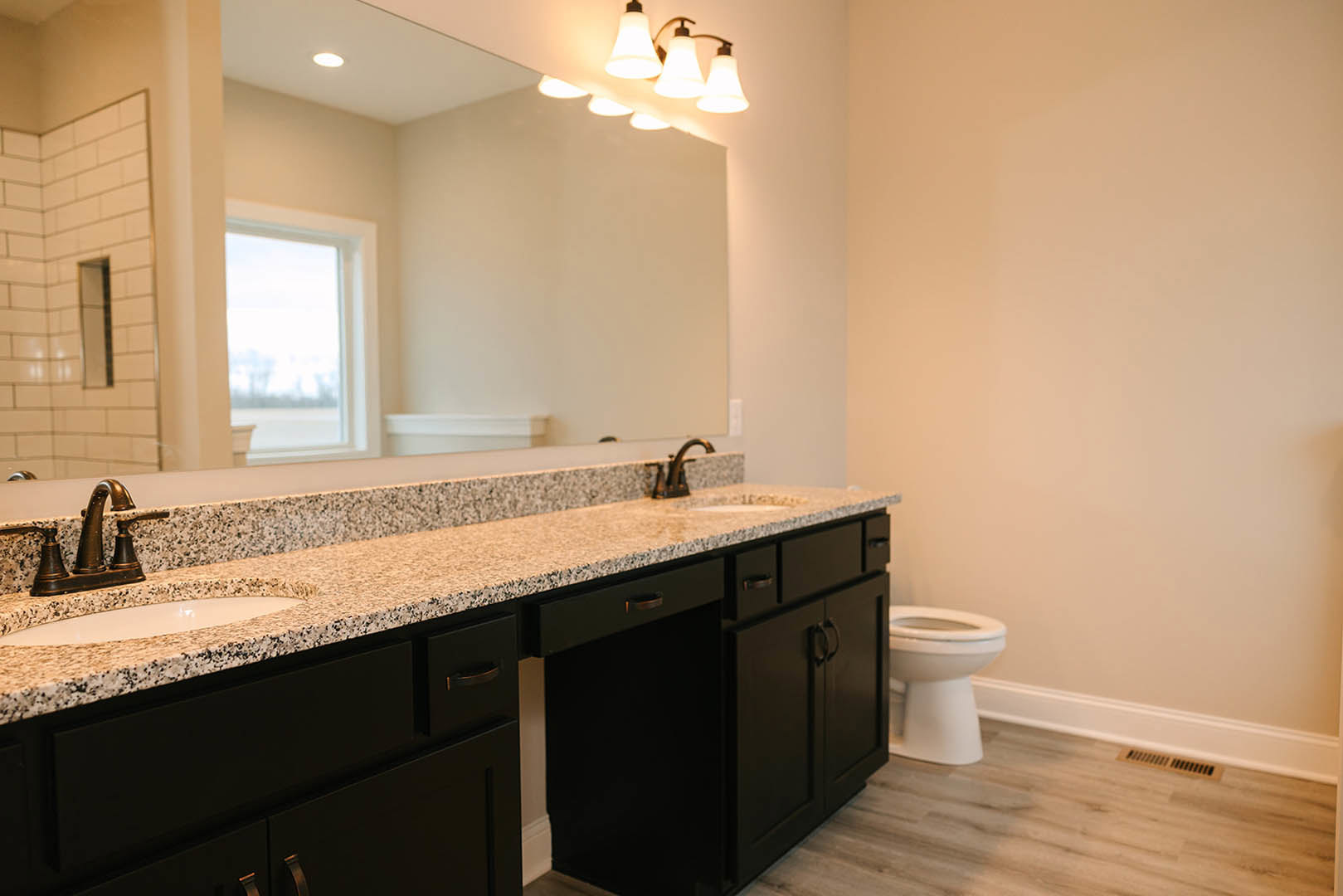 Bathroom with wide framed mirror above quartz countertop, undermount sink, chrome faucet, white cabinetry, wall-mounted light fixtures, and neutral tile backsplash.