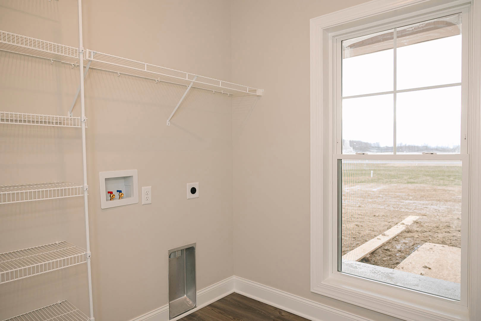 Bathroom with plaster walls, white shelf, window with white frame overlooking a field, black circular fixture, white square panel with red and blue valve, metal corner trim with