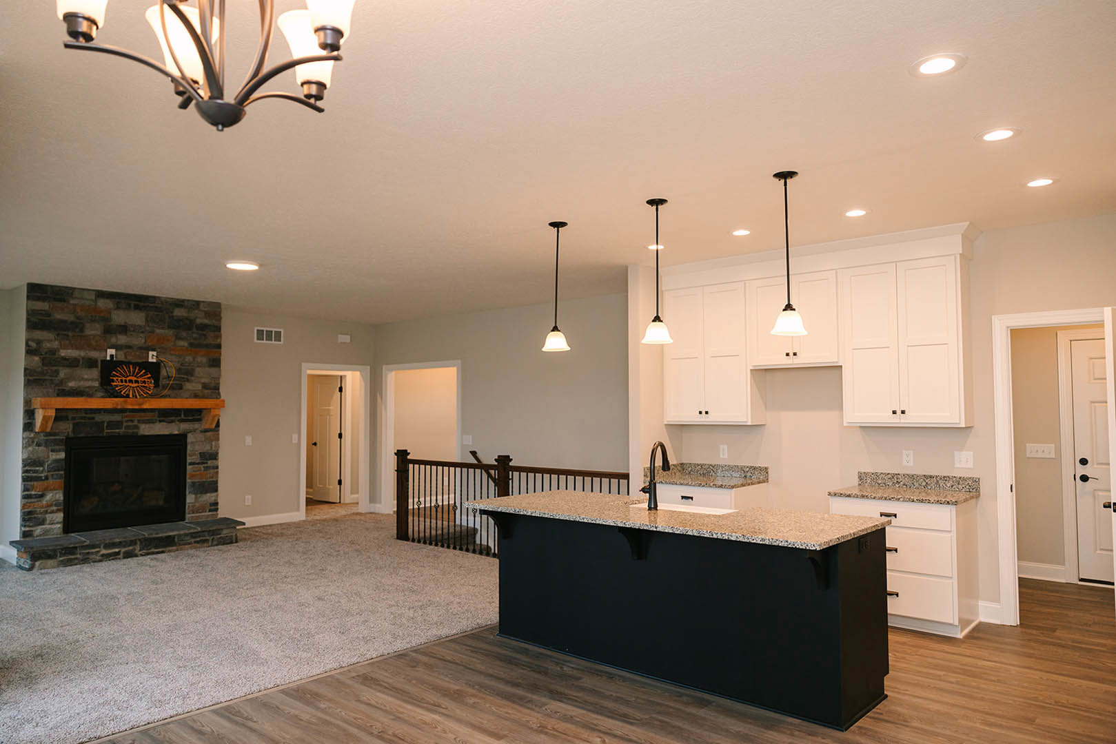 Kitchen with black countertop, stone fireplace featuring glass window and wood mantel, white door with black knobs, close-up of black lamp and light fixture, cabinetry and flooring