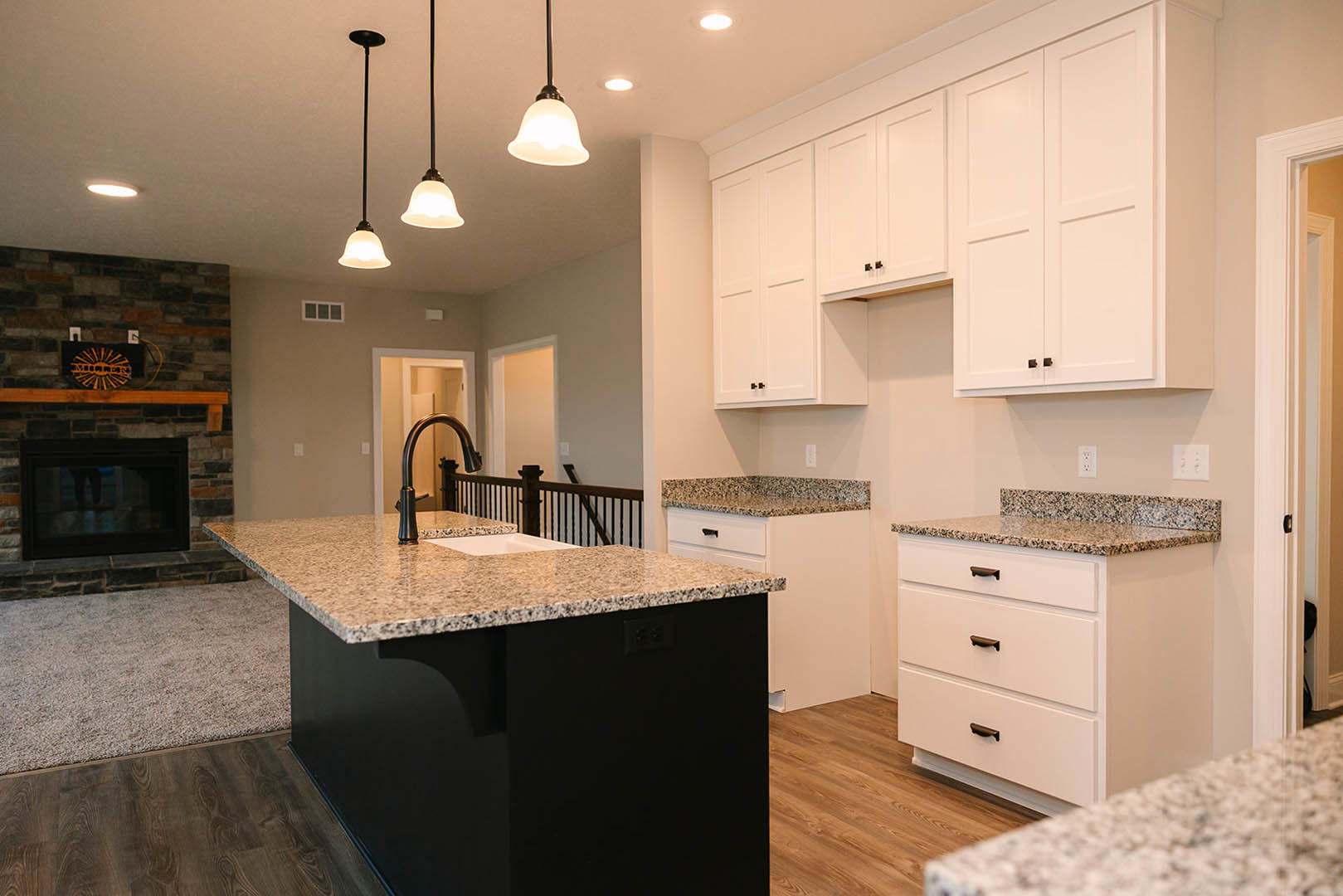 Kitchen with black island featuring built-in sink, white cabinets with black handles, white walls, and a person standing near the island