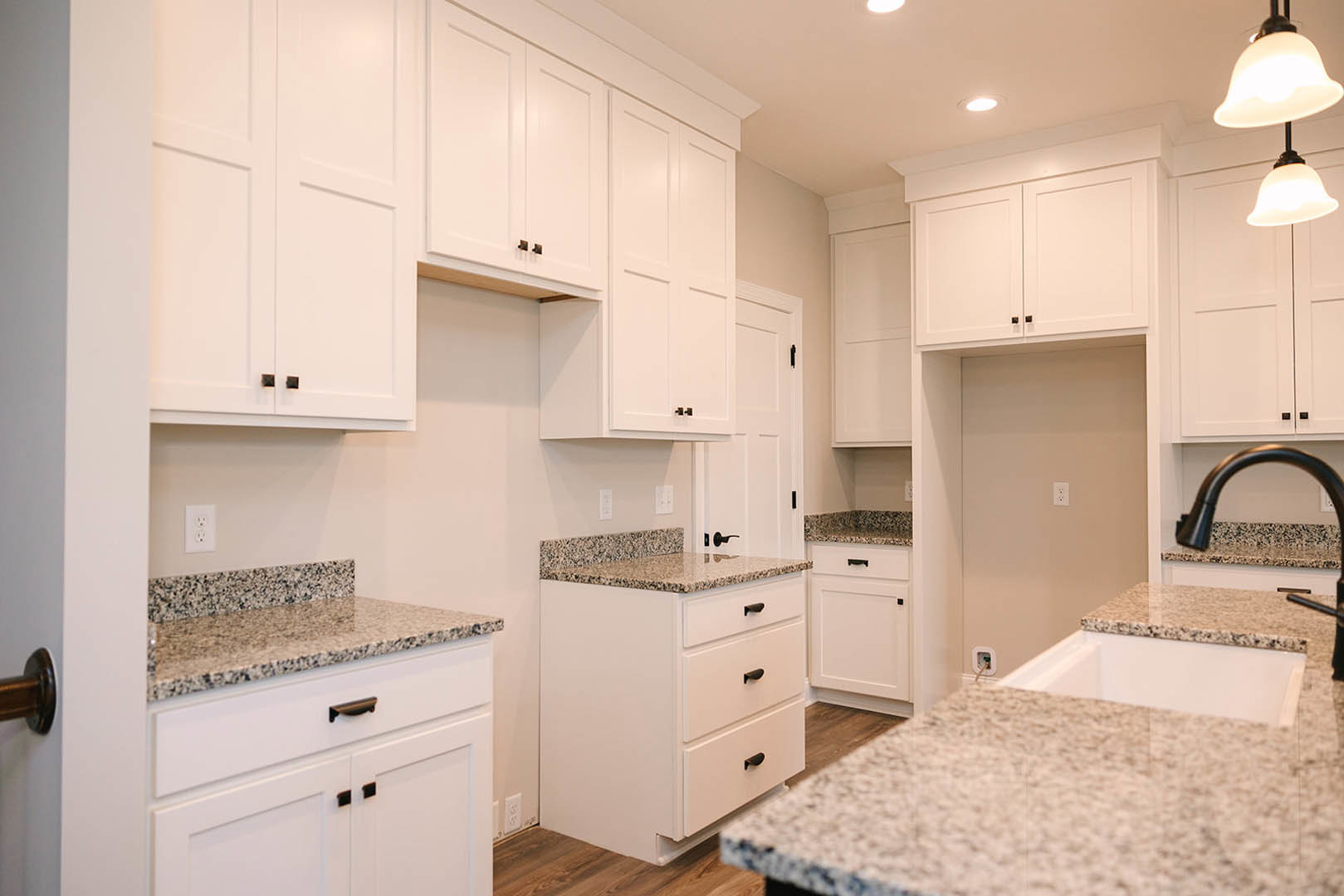 White kitchen cabinets with black handles, granite countertops, stainless steel sink, and drawers; close-up views of countertop, lamp, and white door.