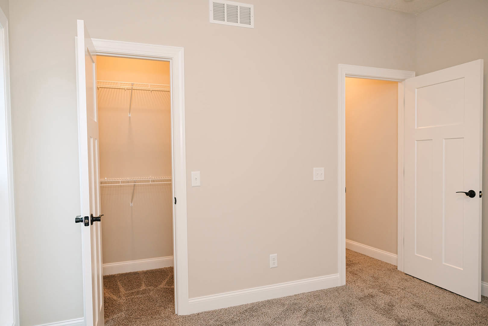 White closet door with matte black handle, white vent above, smooth plaster walls, light wood flooring