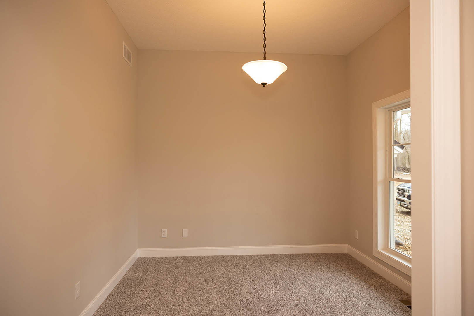 Neutral-toned room with white plaster walls, laminate flooring, ceiling light fixture with chain, and window overlooking driveway with parked car