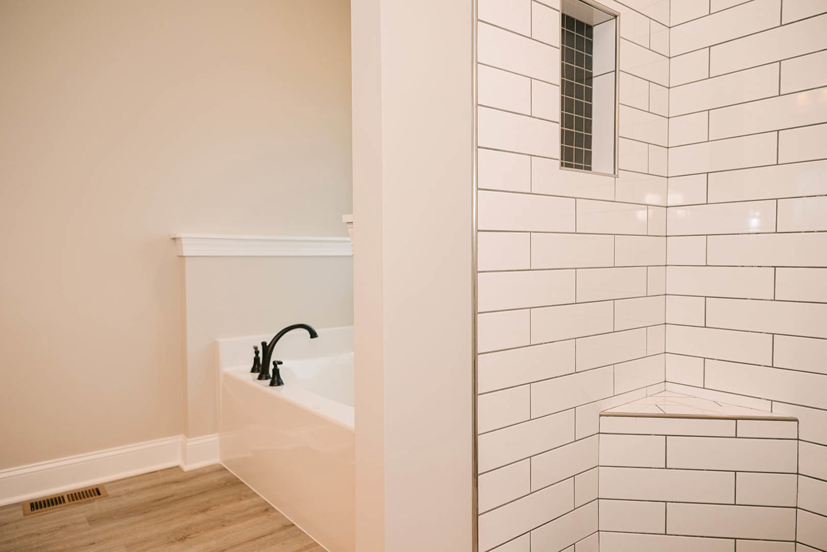Bathroom featuring a freestanding tub, glass-enclosed shower with built-in bench, tile walls, wall vent, wood flooring, chrome faucet, and window providing natural light