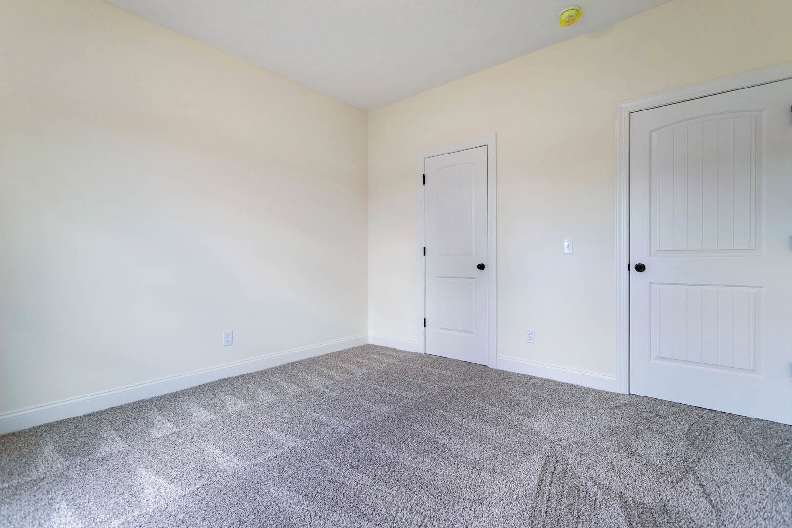 Carpeted room with white walls, two white doors featuring black hardware, one door with a curved top, yellow object on a white surface