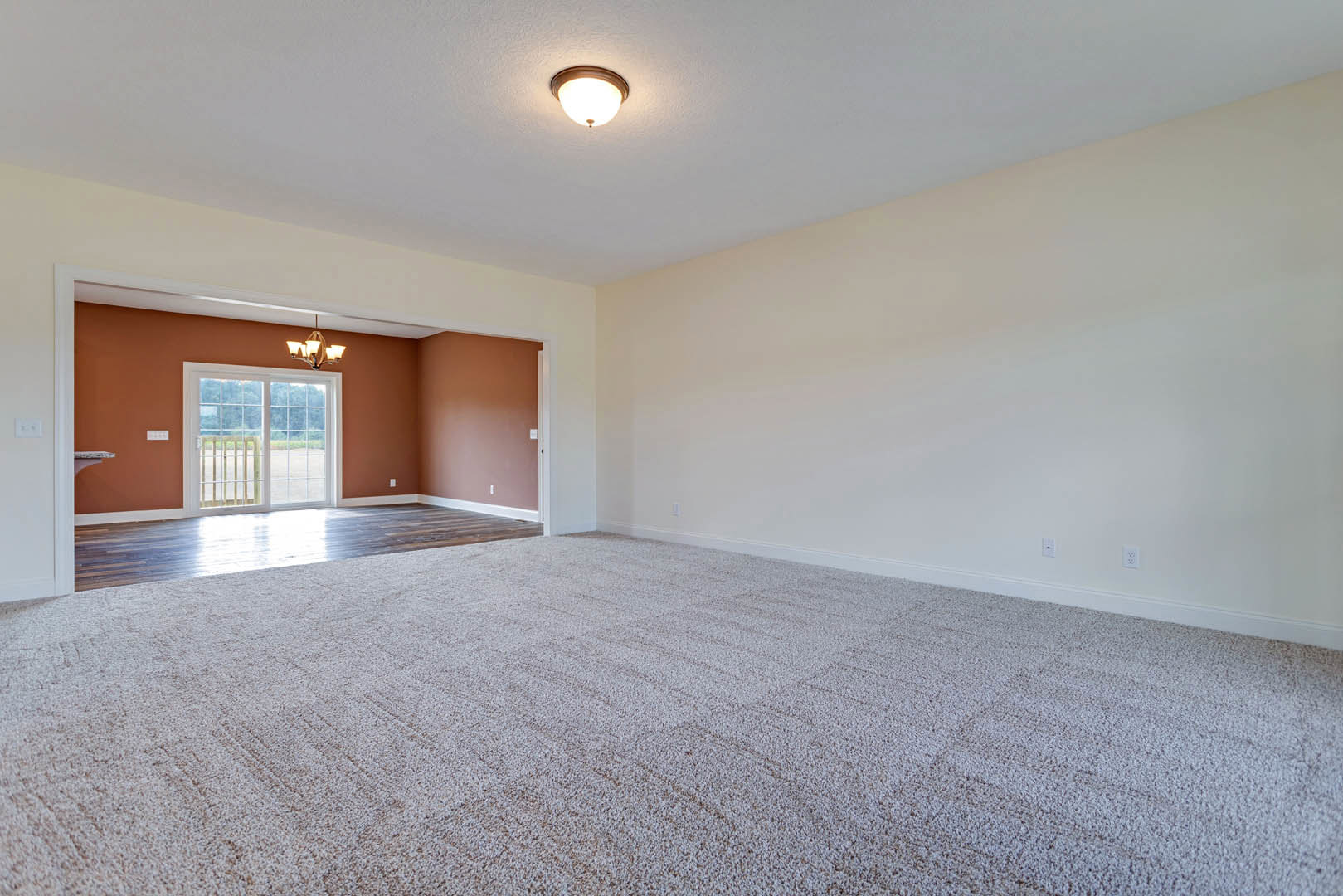 Empty room with white carpet, sliding glass door, white walls, ceiling light fixture, and crown molding