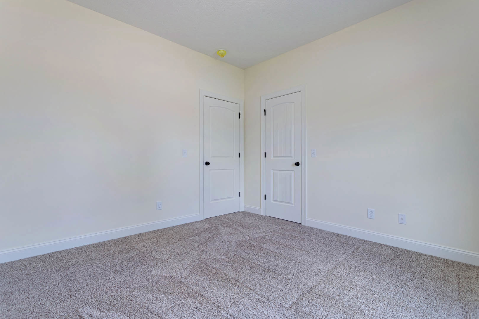 Carpeted floor and walls in a room with two white doors featuring black knobs, white ceiling with recessed yellow light