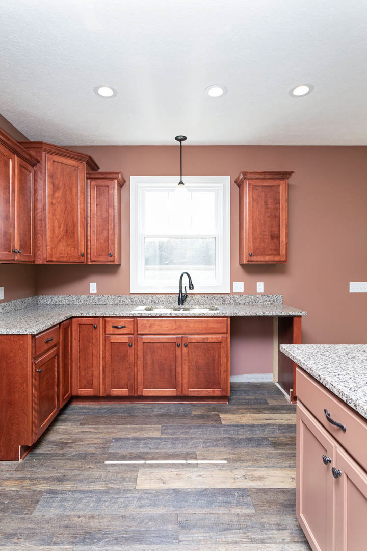 Granite countertops and wood cabinetry in a kitchen with a pendant light above the window, wooden flooring with integrated light strip, close-up views of a wood door and kitchen