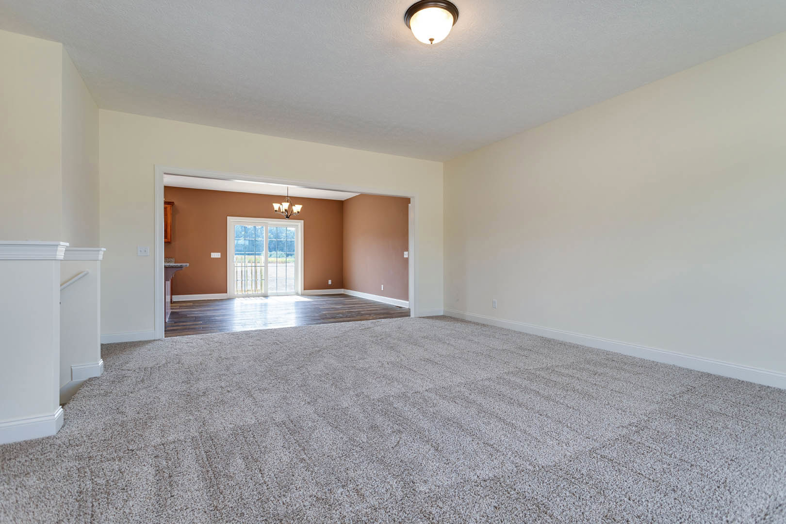 Carpeted room with white walls, paneled door, ceiling chandelier, window with trim, and hardwood floor visible in adjacent space