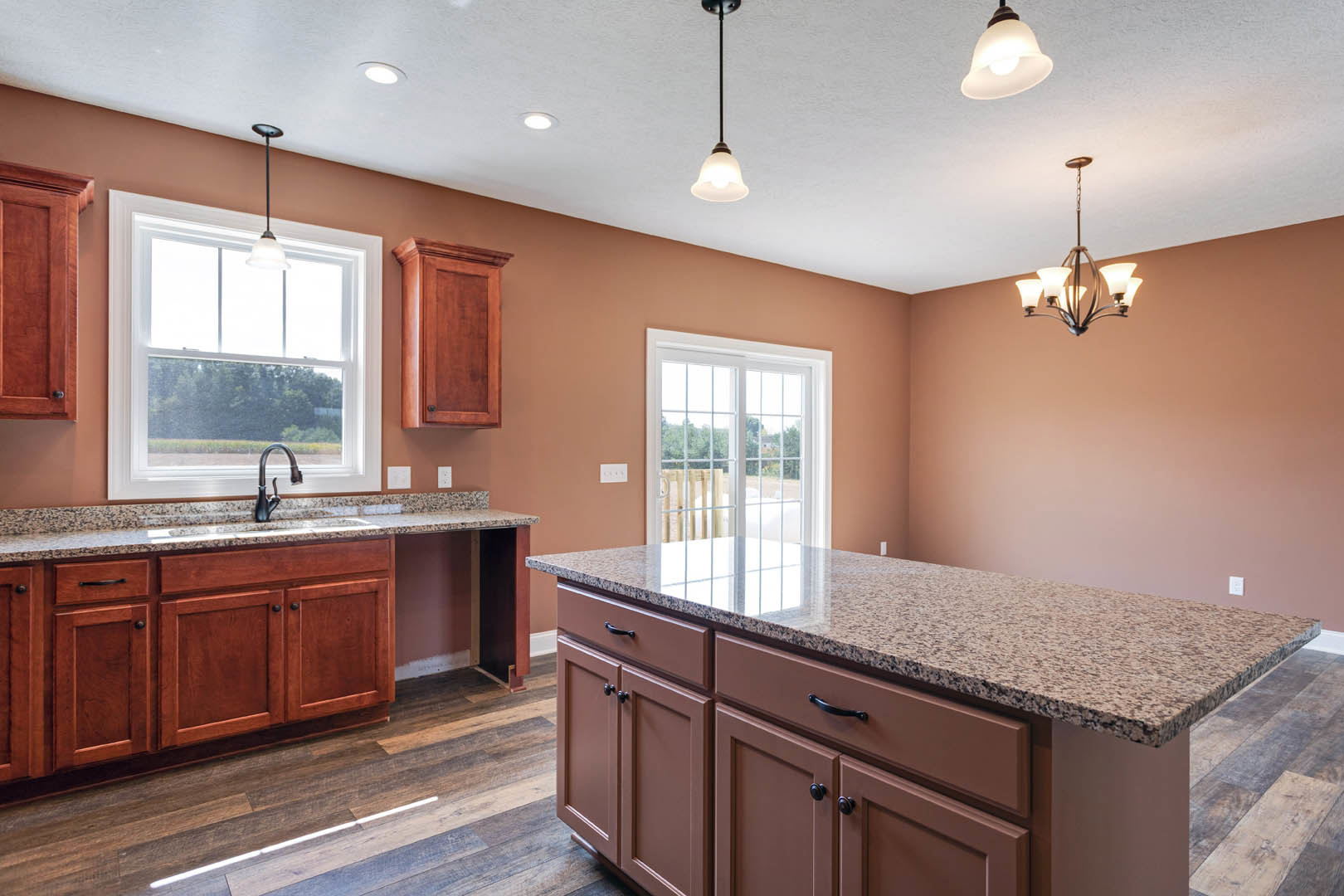 Marble countertop kitchen with undermount sink beneath a window, white cabinetry, glass-paneled door, and pendant light fixture
