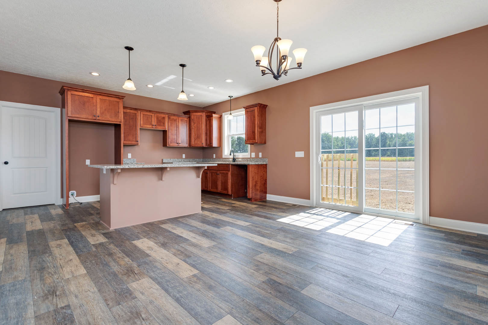 Open kitchen with wood flooring, white cabinetry, bar seating at a quartz countertop, sliding glass door overlooking a grassy field, white interior door with black handle, black