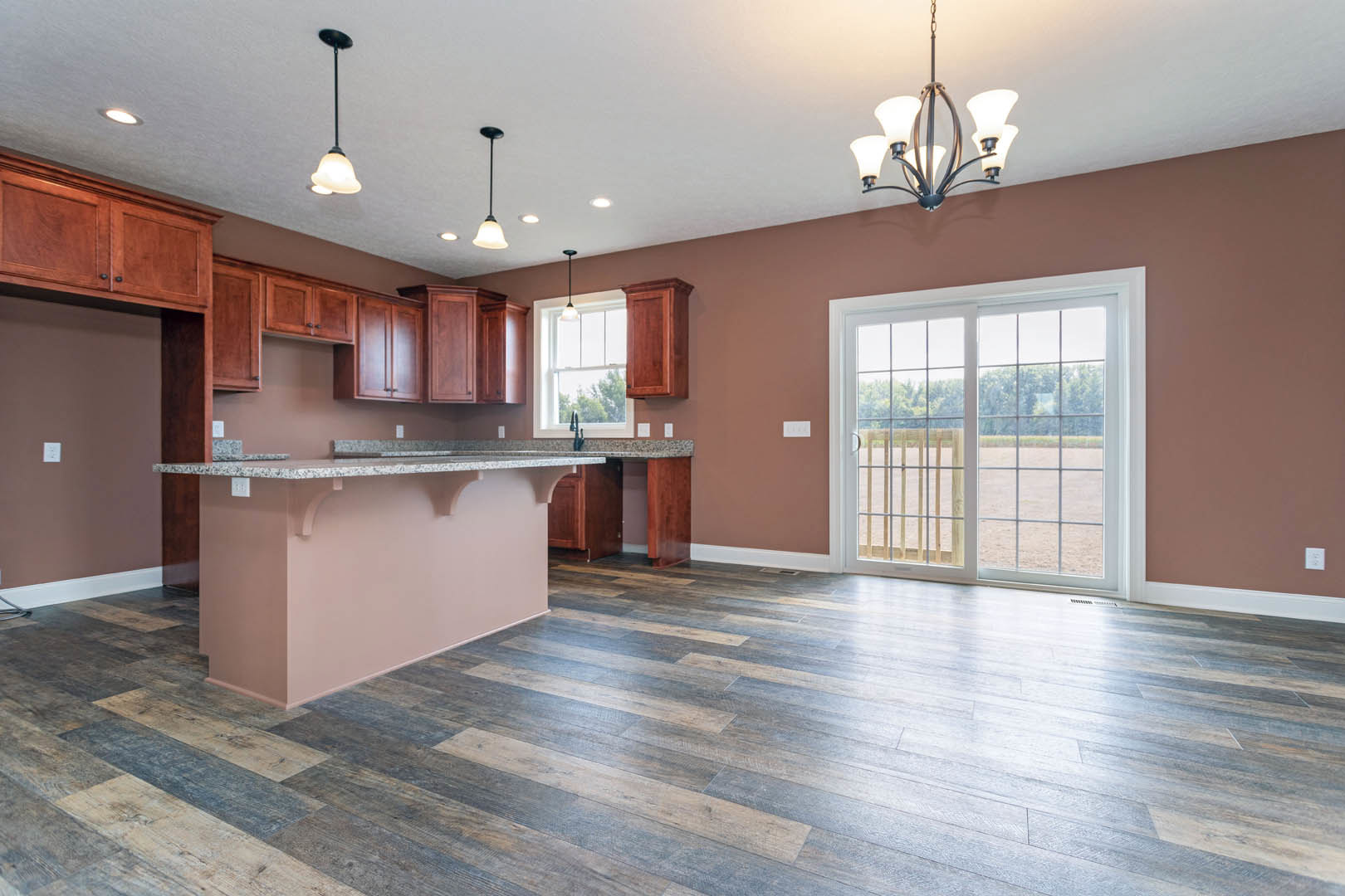 Open kitchen and living room with wood flooring, white cabinetry, stone countertop, sliding glass door leading to fenced backyard, wood paneled accent, modern chandelier, stainless