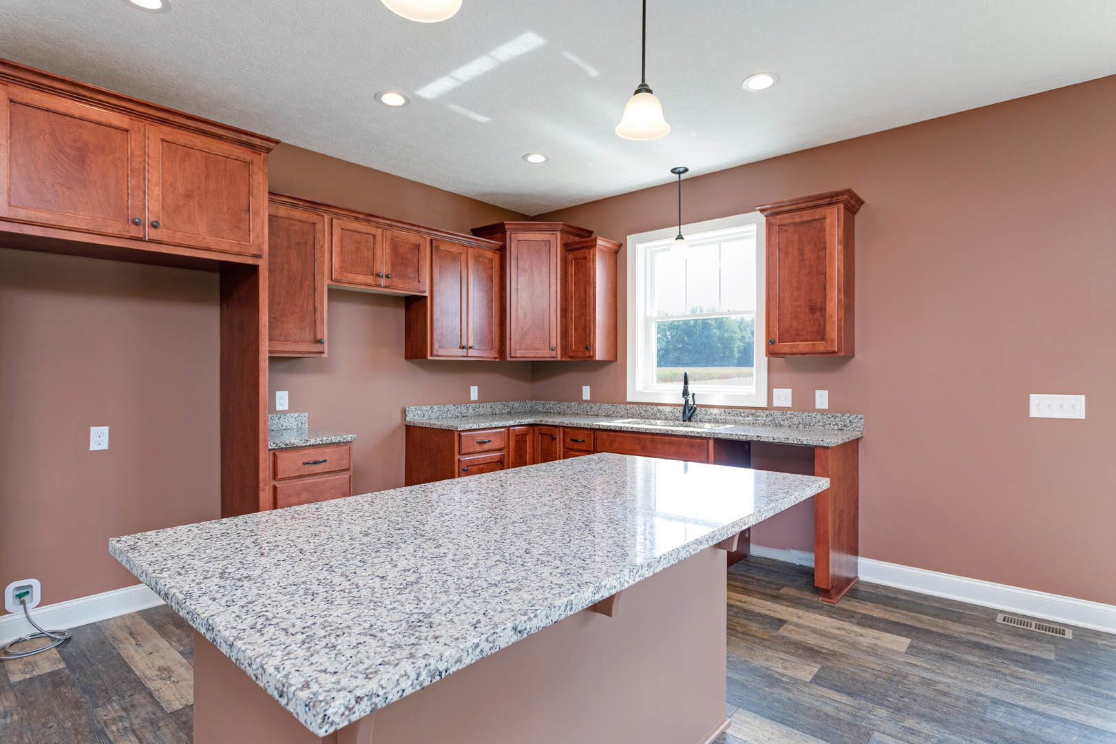 Granite countertops and wood cabinets in a kitchen, stainless steel sink, tile backsplash, overhead lighting, window, and built-in appliances