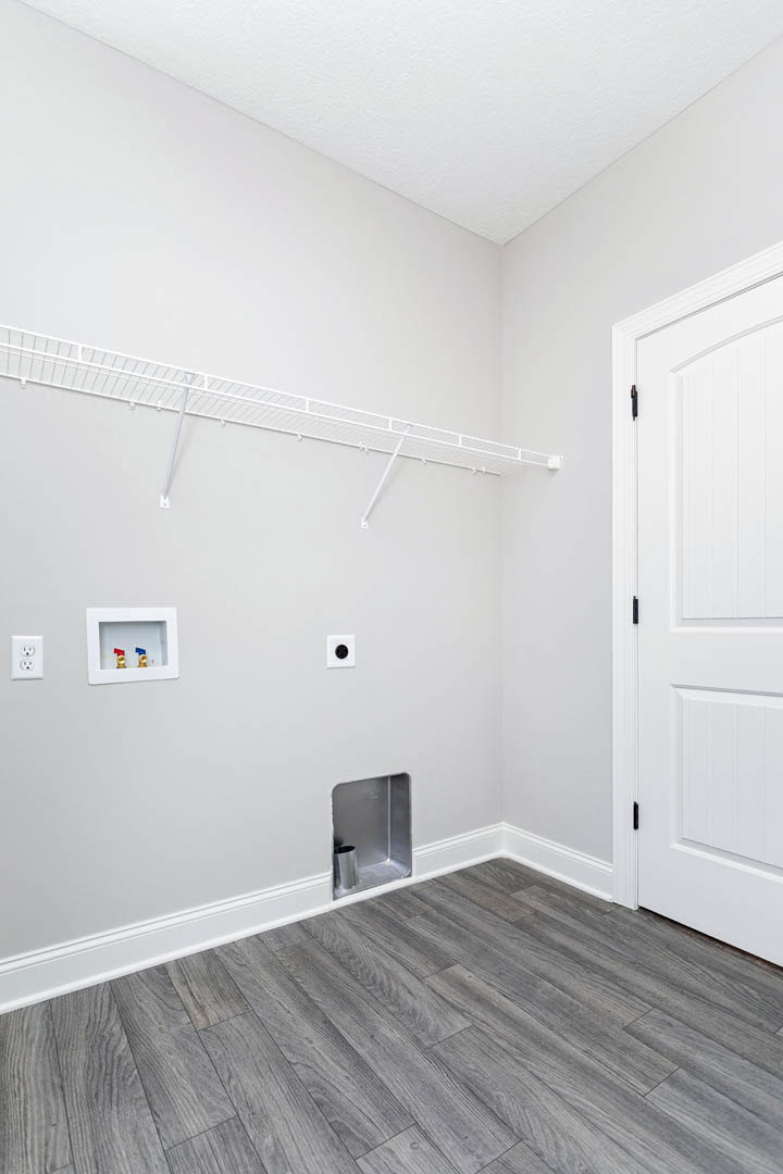 White plaster wall with built-in white metal shelf, recessed utility box with red and blue valves, close-up of white door, silver can in corner, wood laminate flooring with metal