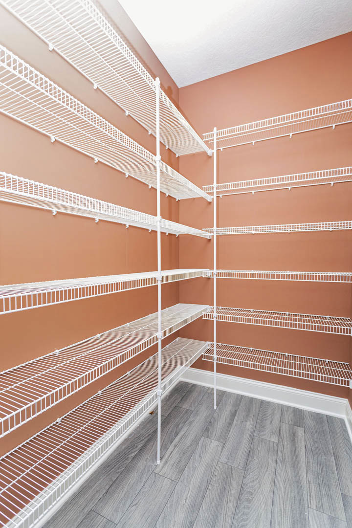 White metal shelving unit against a wall, wood flooring, white and brown ceiling, close-up of shelf and floor details.