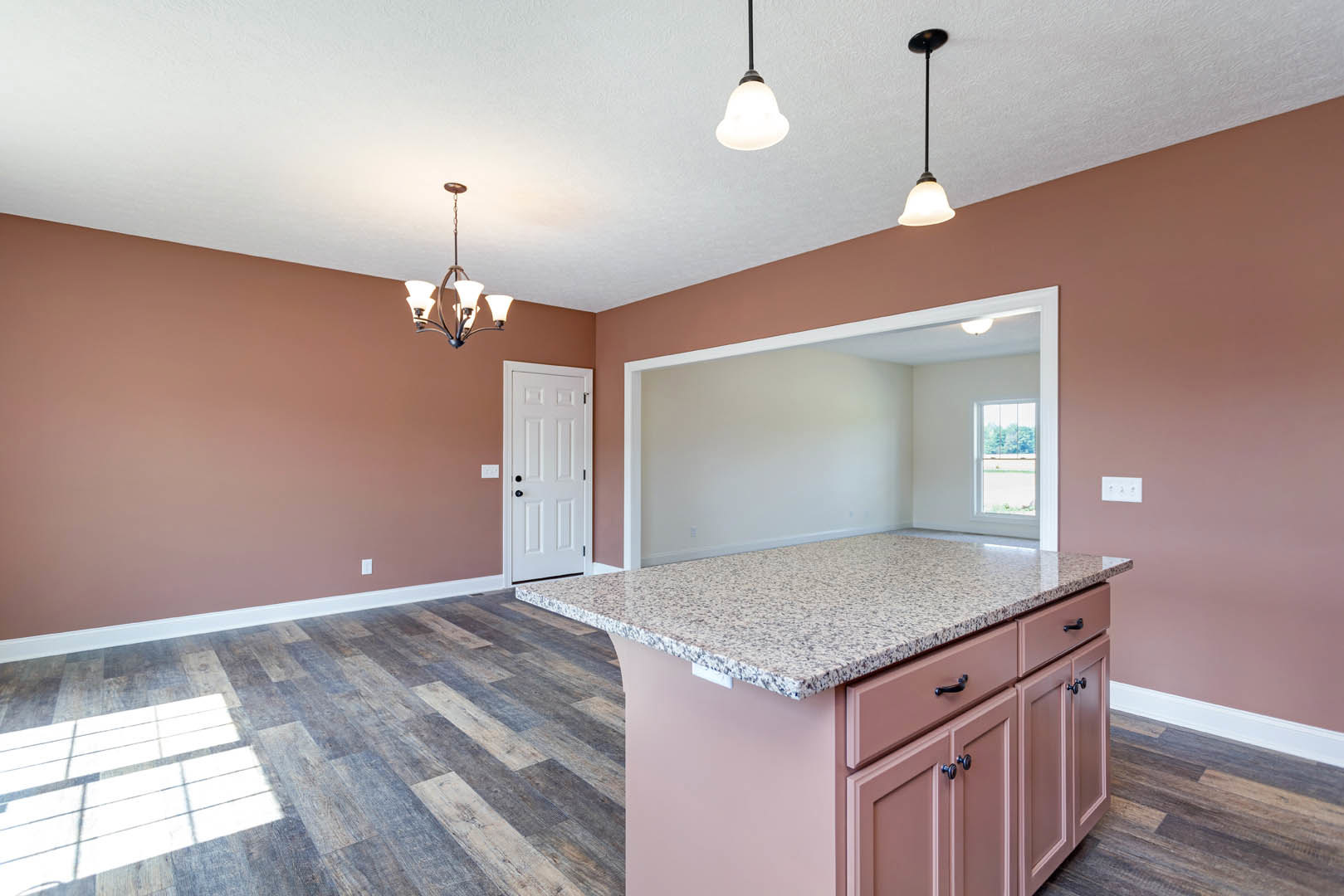 Marble countertop kitchen with pink lower cabinets, white door featuring black knobs, black support pole, tile backsplash, and chandelier overhead