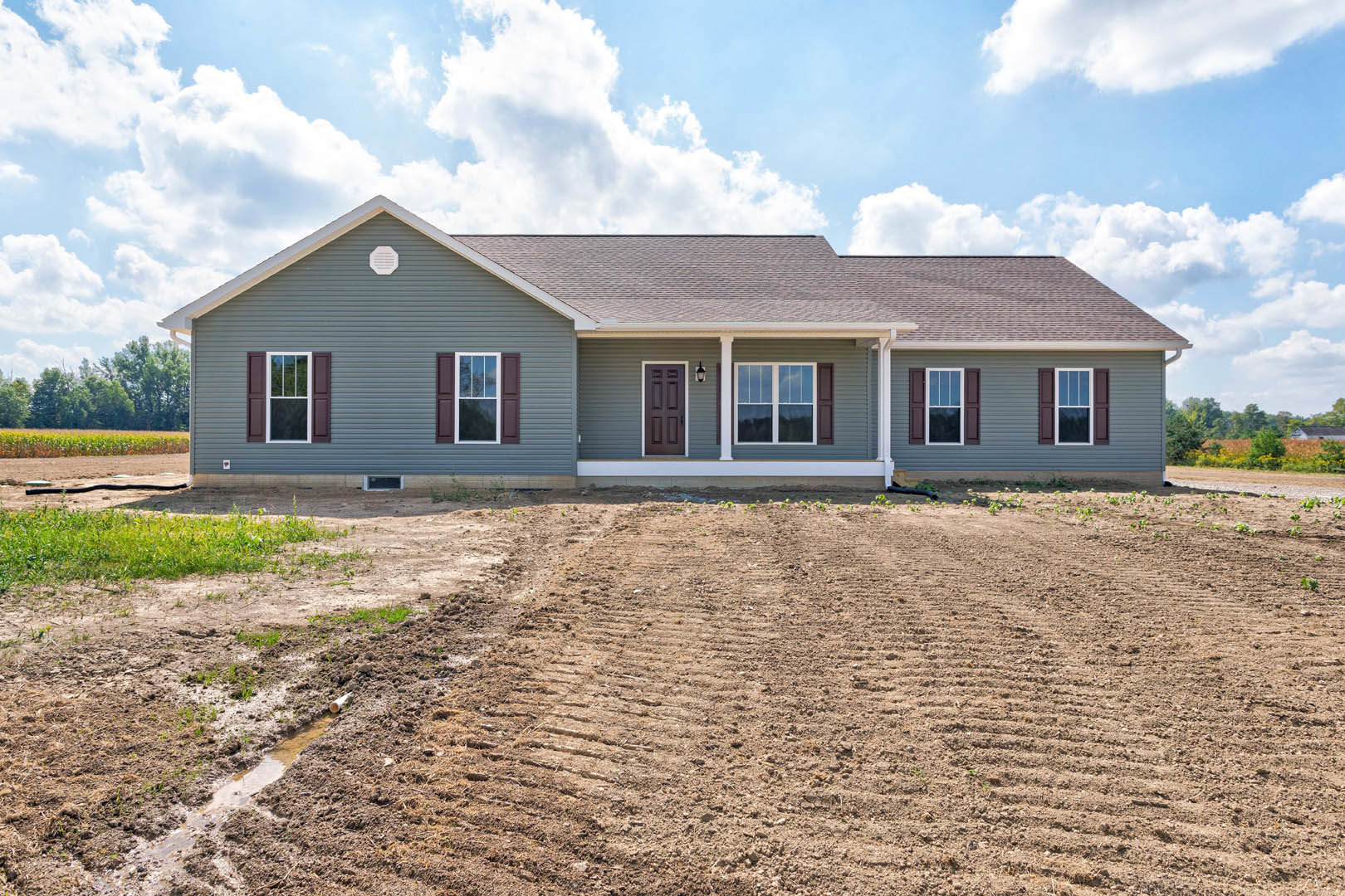 White custom home with front porch, white-framed windows, and door, set beside a dirt field under a blue sky.