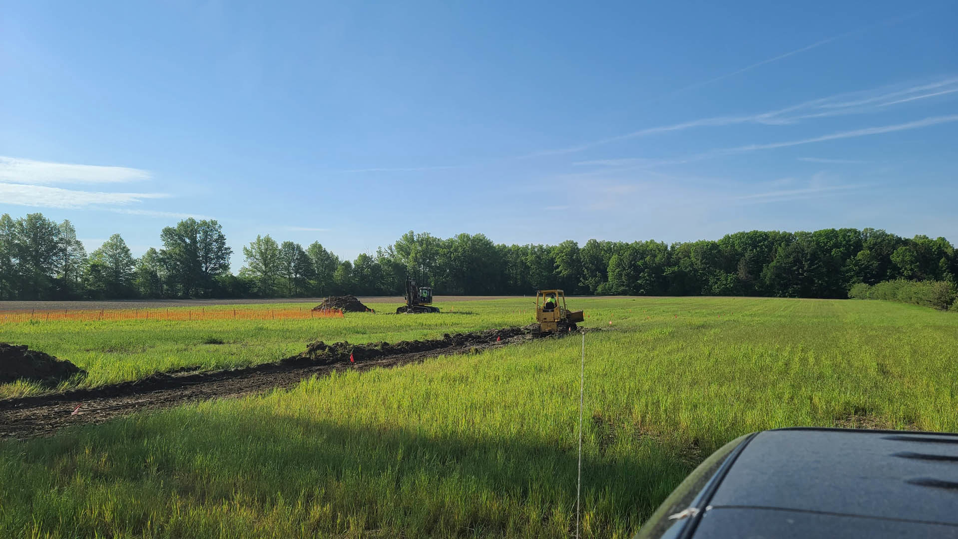 Green tractor parked on grassy field under blue sky with scattered clouds, surrounded by trees and plants