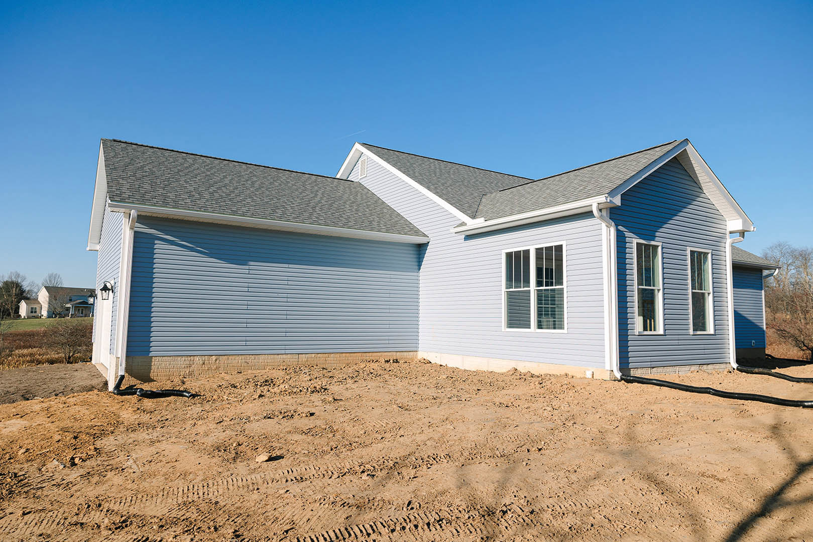 White-framed window set in light siding, blue roof overhead, dirt ground with tire tracks in front of house under construction