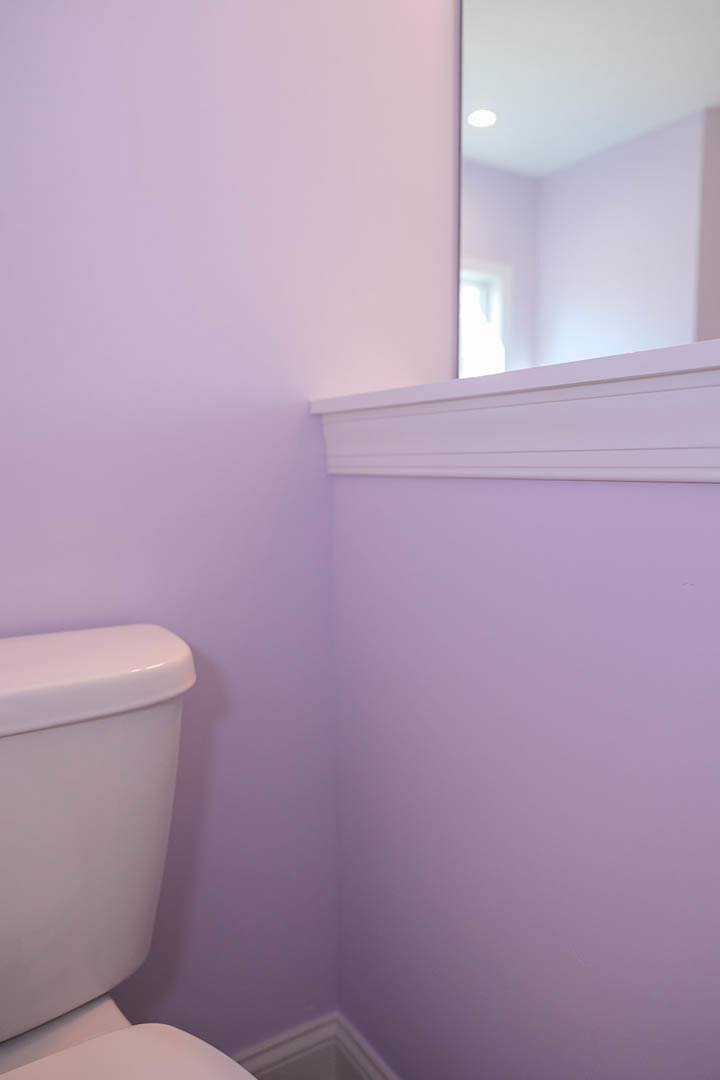 White toilet with closed lid beside a rectangular wall-mounted mirror in a bathroom with light-colored walls
