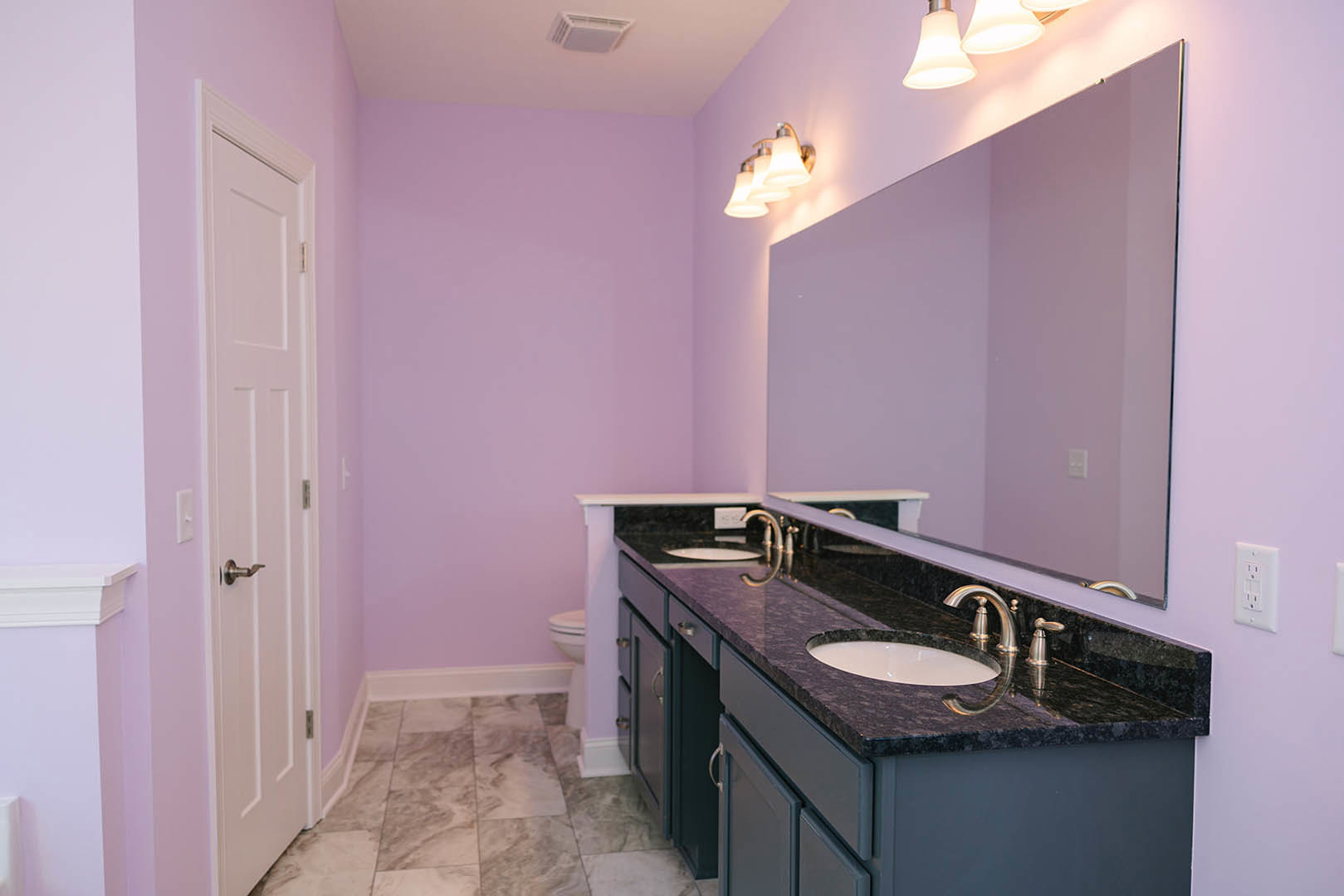 Bathroom with deep purple painted walls, large rectangular mirror above a granite countertop, white sink, chrome faucet, and white cabinetry