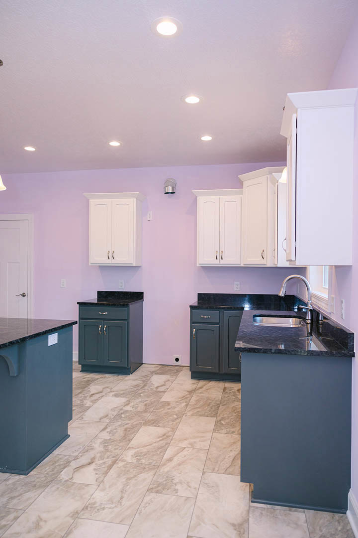 Purple kitchen walls, white cabinets, black drawer cabinet, tile floor, white door with square panel, blue box on countertop, stainless steel sink