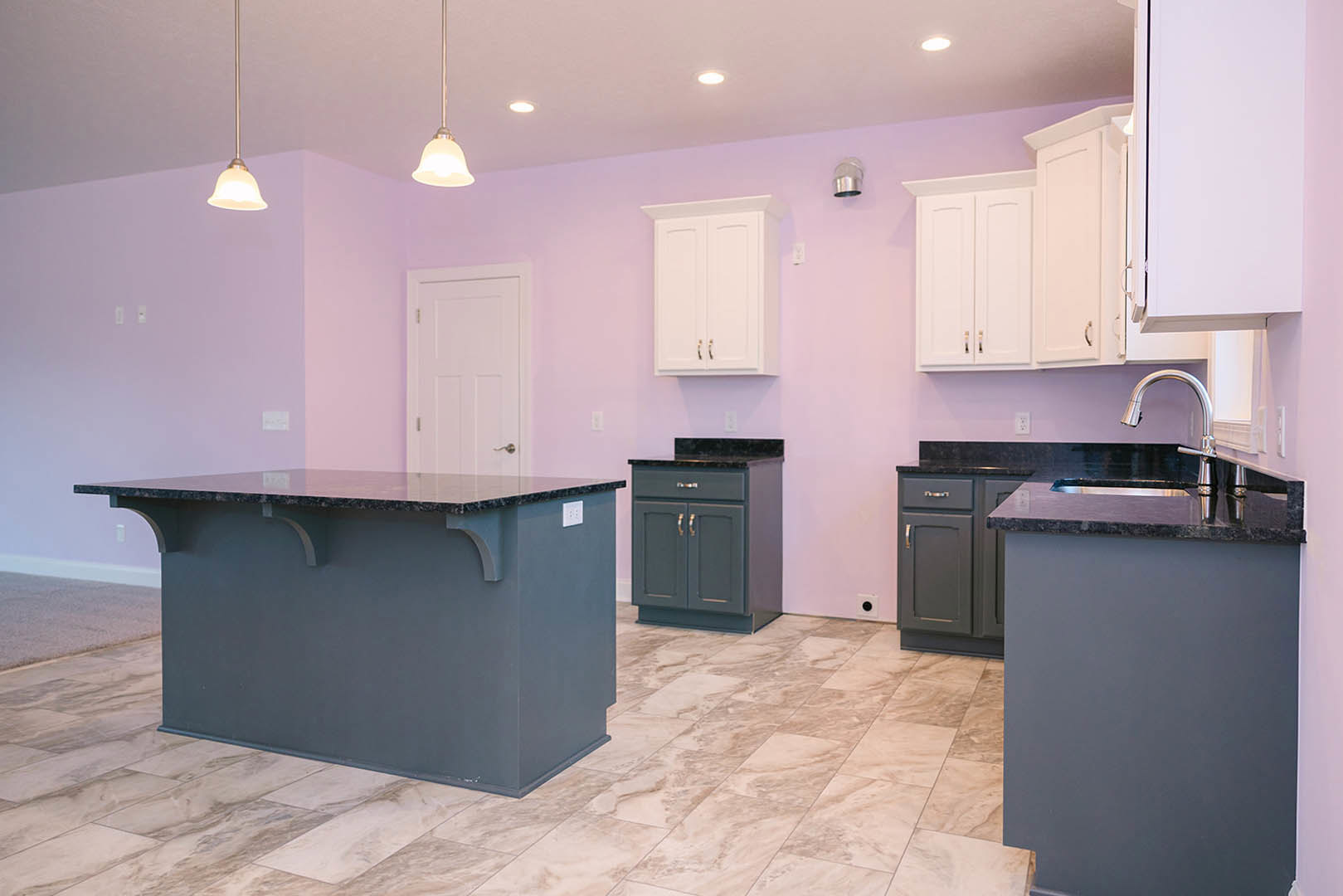 Purple kitchen walls, white cabinets with gold handles, marble countertops, stainless steel sink, white door with silver knob, light wood flooring