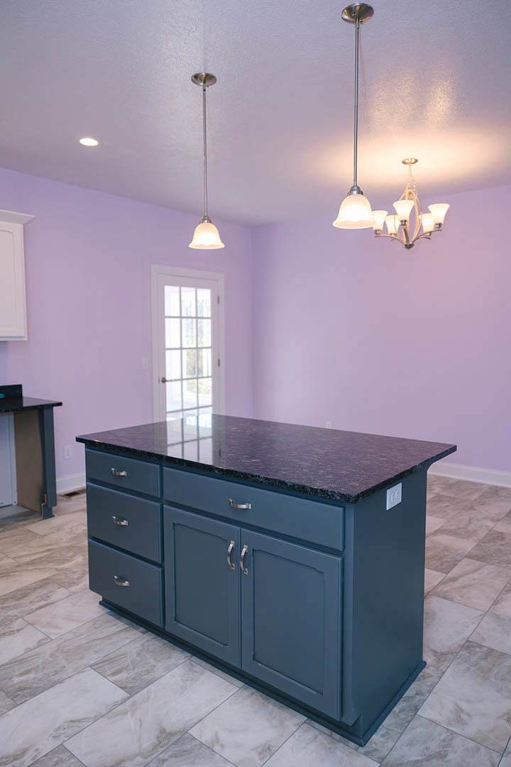 White kitchen island with shaker cabinets and drawers, light stone countertop, hardwood flooring, and neutral walls in a spacious kitchen.