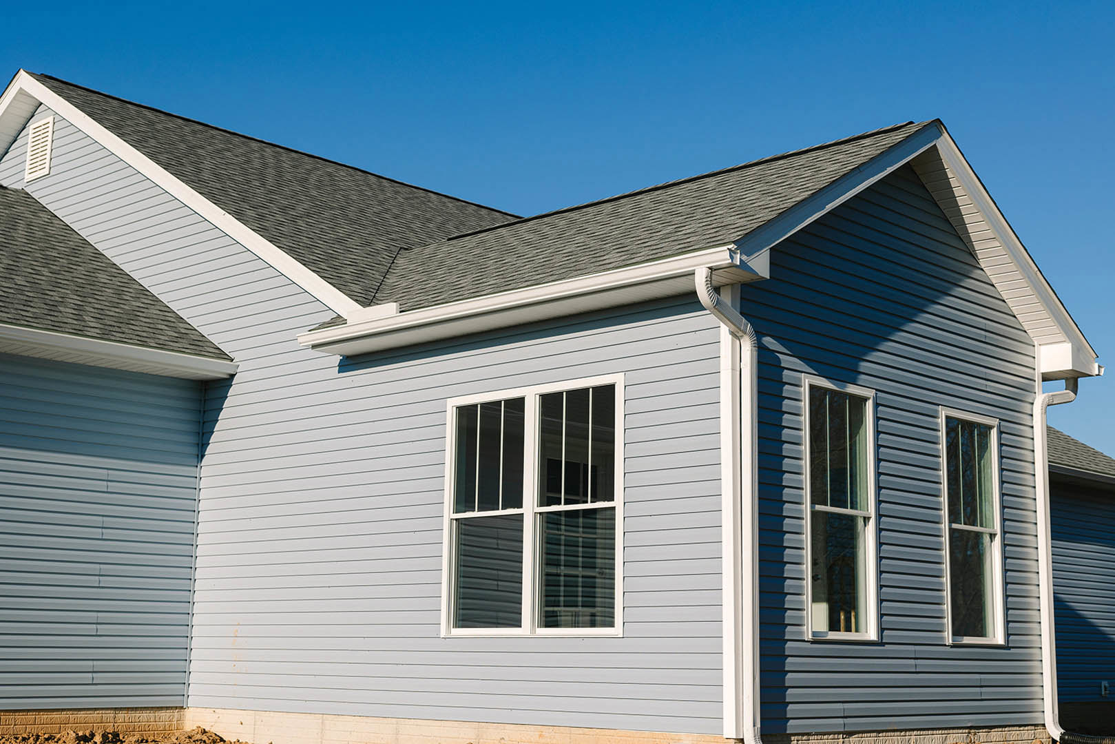 Blue metal roof with white gutters, light-colored siding, and white-framed sash windows with bars on a residential cottage exterior