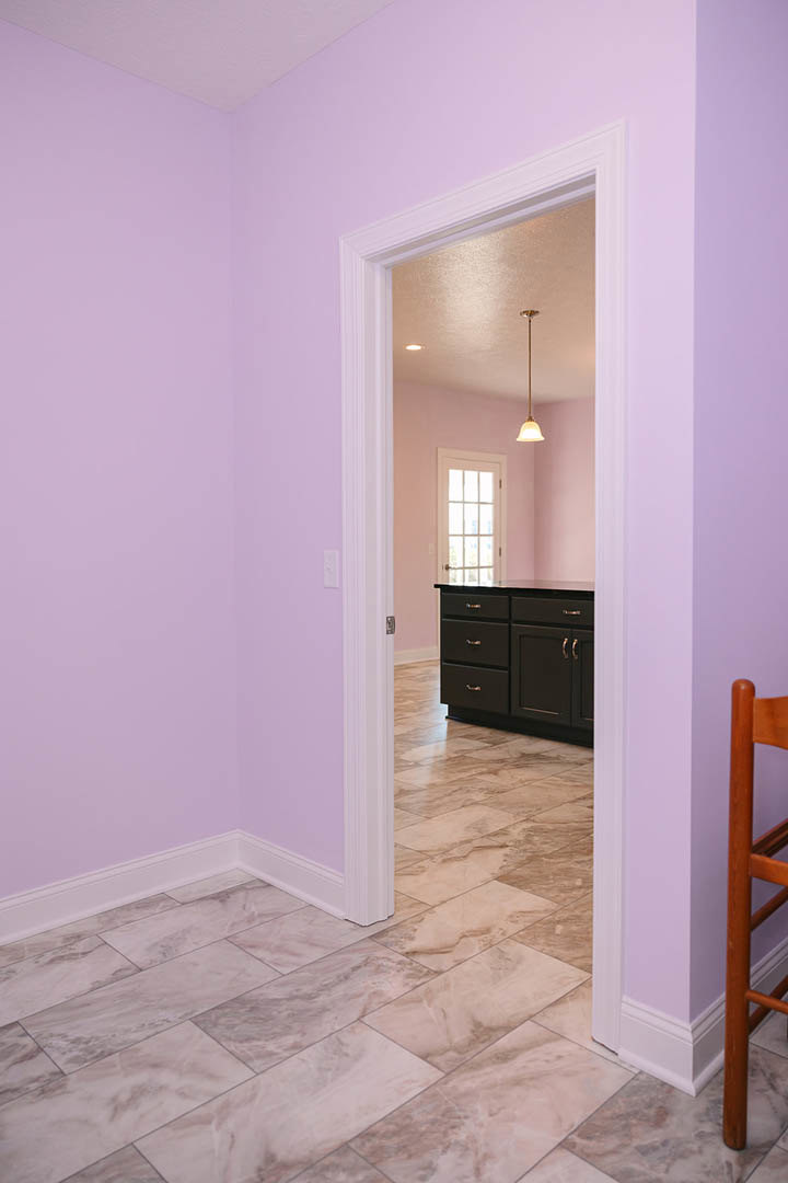 Purple-walled room with a black kitchen counter, multi-pane window, and a door opening; wooden chair leg and white wall visible in foreground