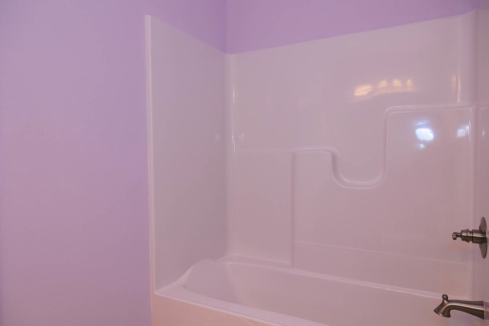 Freestanding white bathtub set against a deep purple wall, chrome faucet and tub fixtures, smooth tile flooring