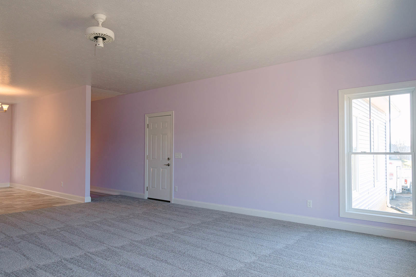 Carpeted bedroom with pink walls, white ceiling, white door with silver handle, window with white frame, and ceiling fan with round light fixture