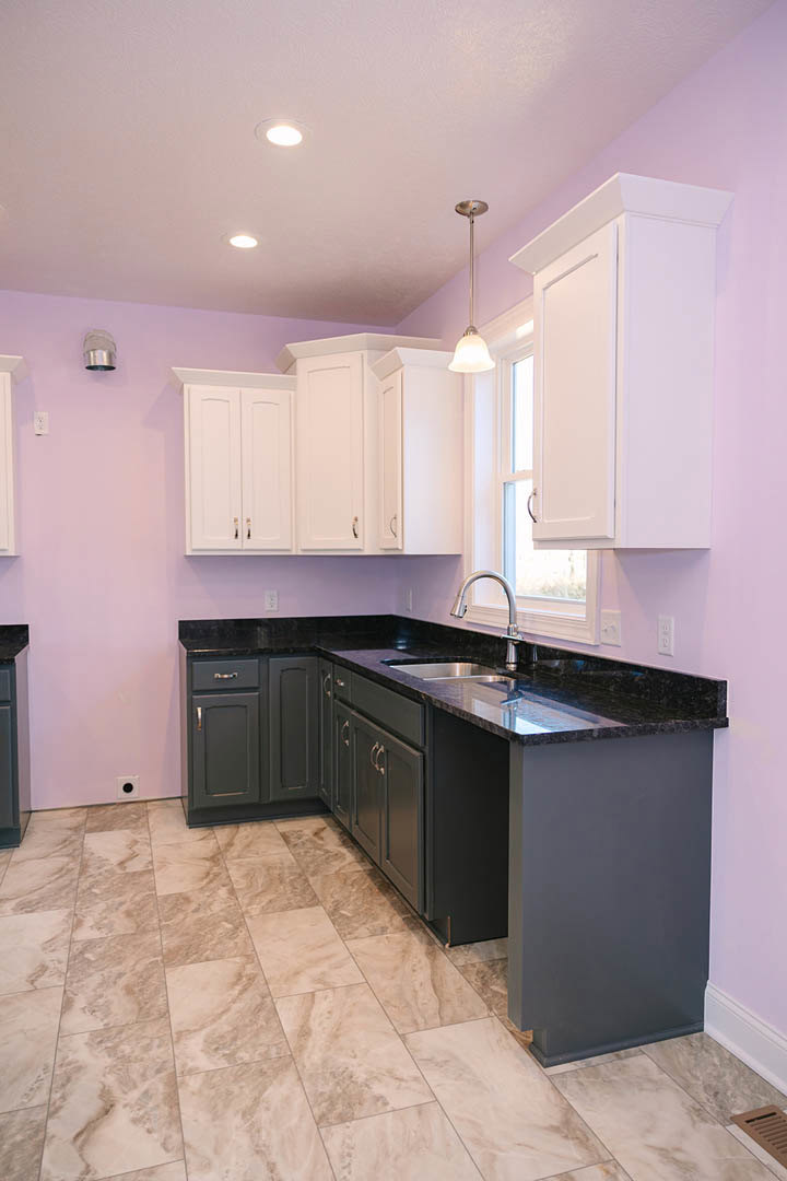 Purple kitchen walls, white cabinets with black countertops, light-colored flooring, stainless steel sink, window above cabinetry, recessed ceiling lighting