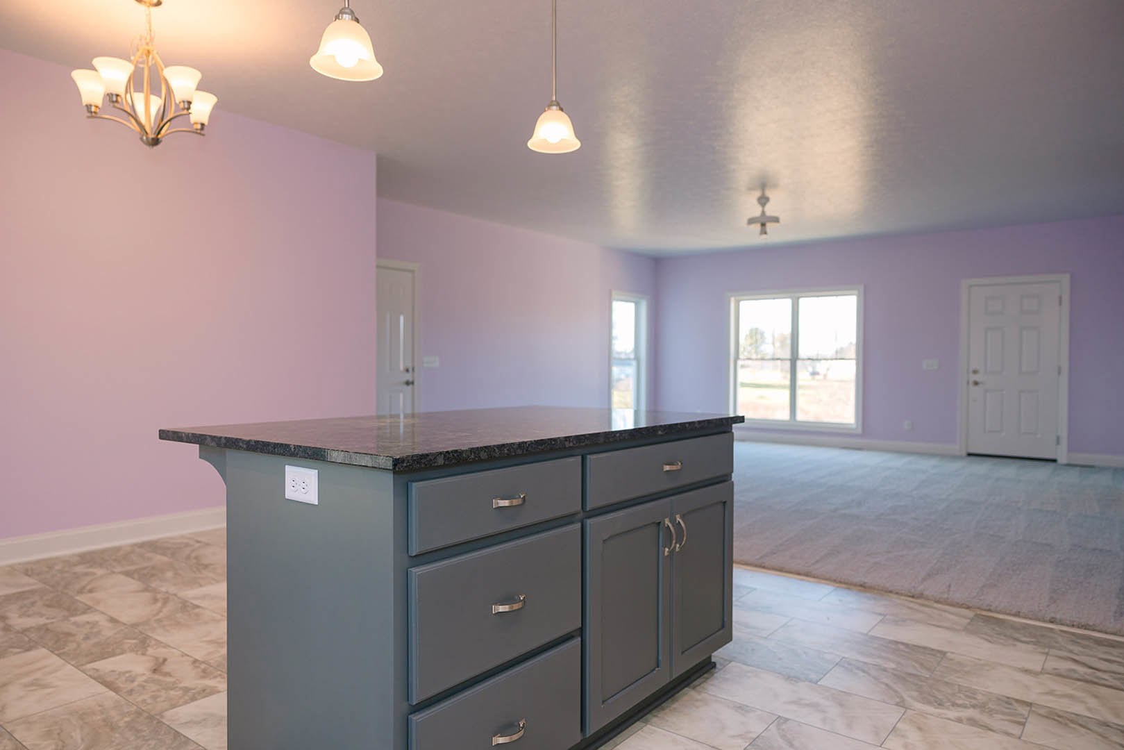 Quartz kitchen island with built-in drawers, gold hardware, white cabinetry, pendant chandelier, window overlooking outdoor greenery, white wall outlet