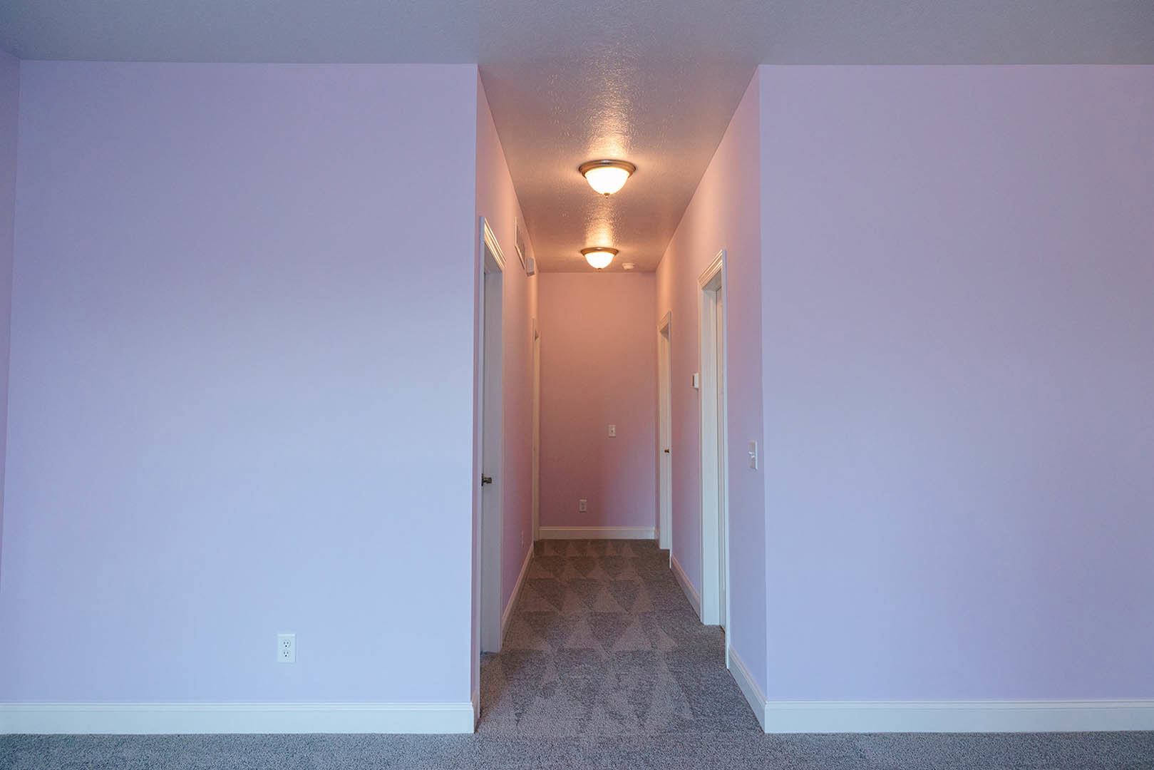 Hallway with white and purple walls, multiple doors, ceiling-mounted light fixture, and light switch on pink accent wall
