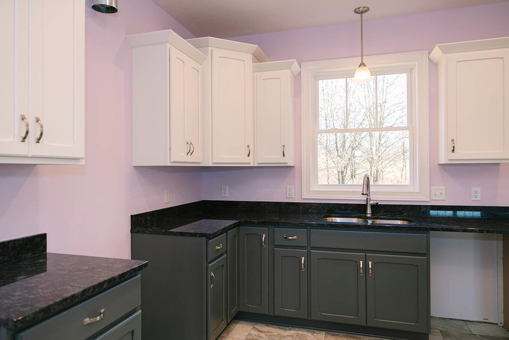 Purple kitchen walls, white cabinets, stainless steel sink beneath window, light fixture on pole, white door, black rectangular appliance with metal frame on countertop