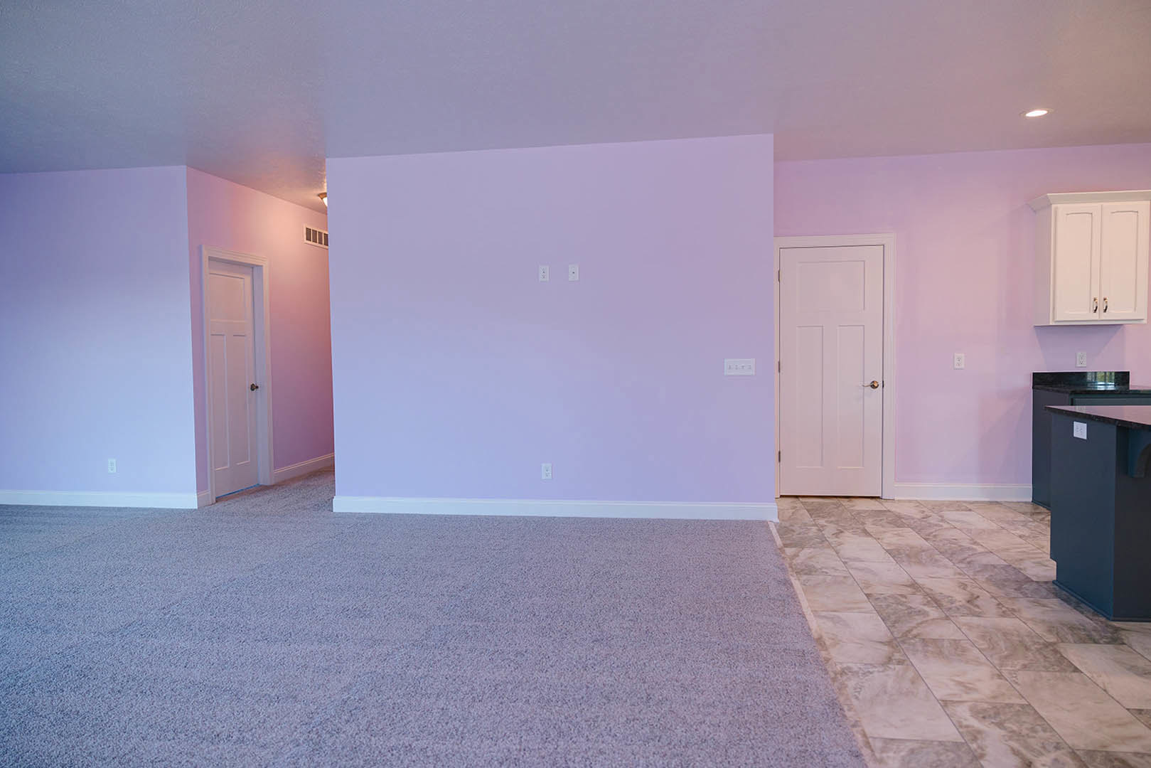 Pink accent wall and purple wall with white switches, white door with gold handle, tile flooring, partial view of blue wall, refrigerator, cabinetry, and waste container in