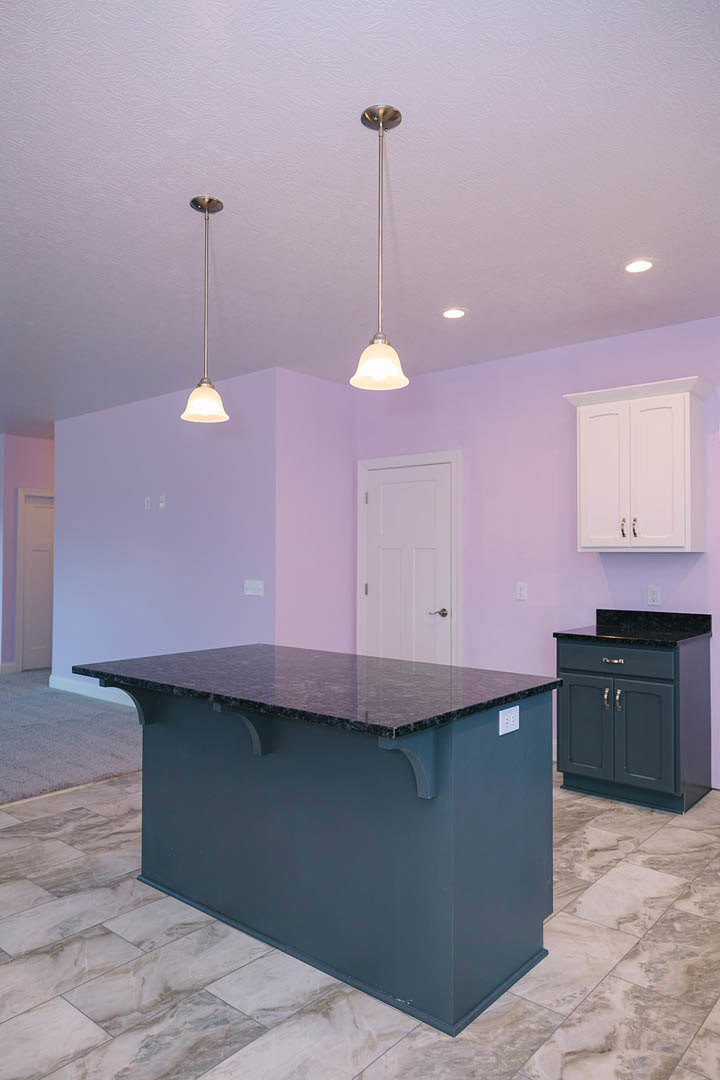 Purple-painted kitchen walls, marble island with matching countertop and floor, white cabinetry with black handles, white door, metal pole near island, recessed lighting overhead.