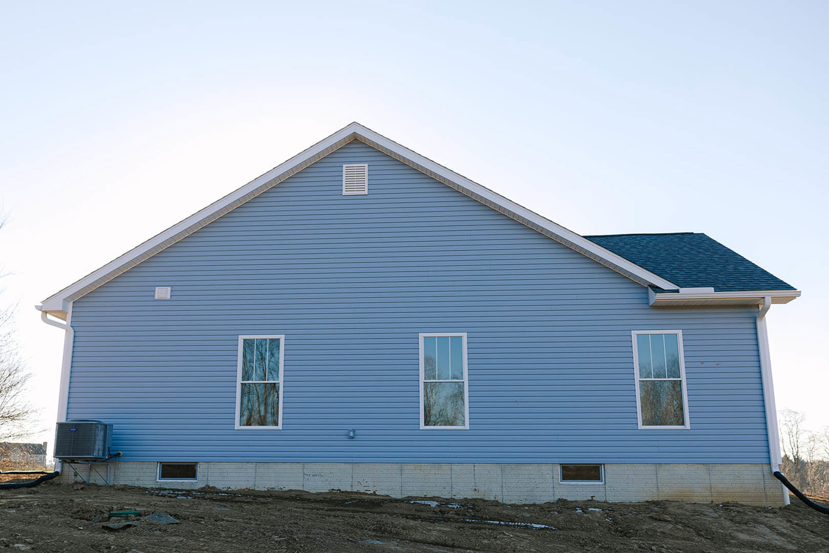 Blue house exterior with white trim, gabled roof, white-framed window reflecting trees, blue siding, and wall vent.