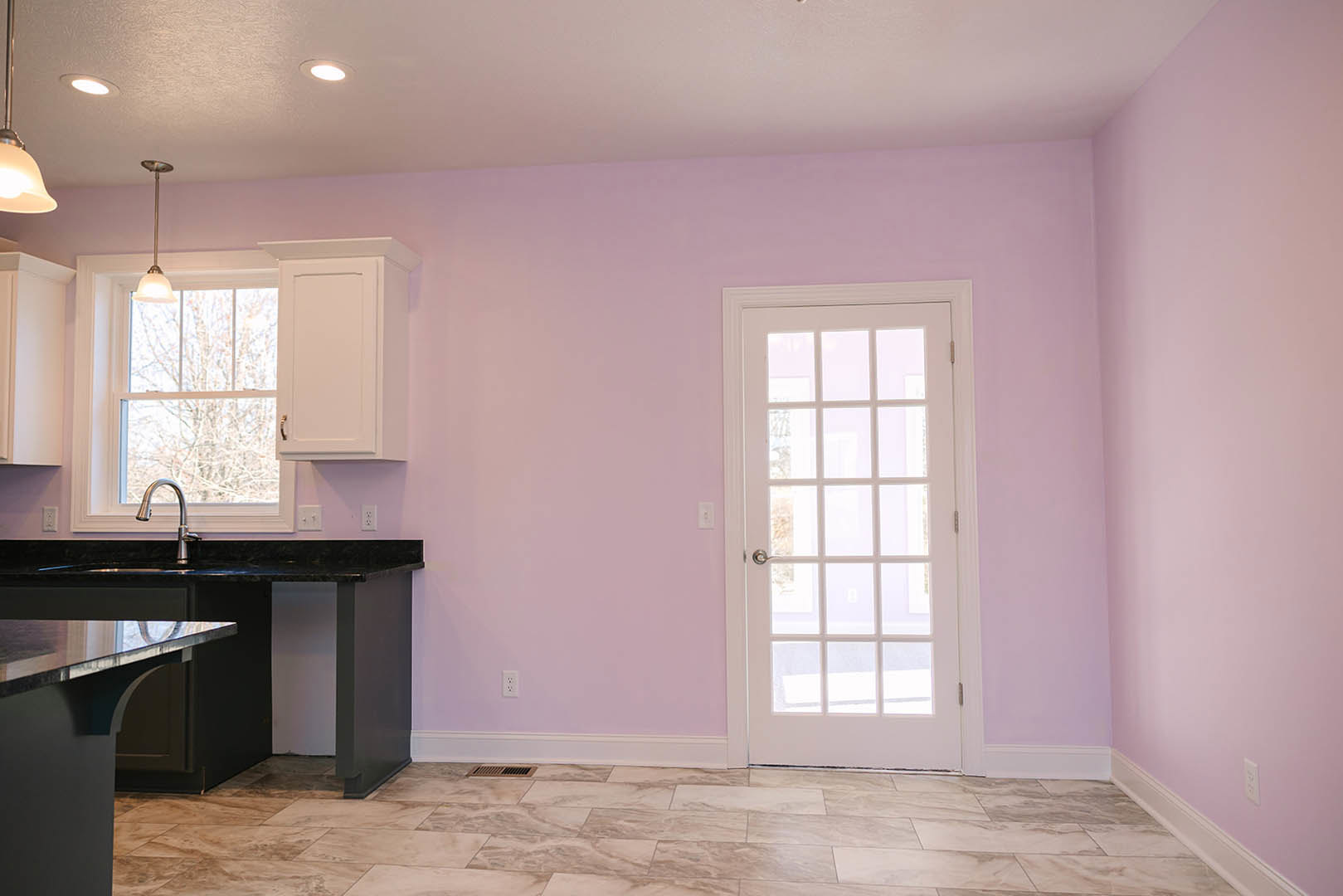 Kitchen with white cabinetry, tile flooring, stone countertop with stainless steel sink, glass-paneled white door, and window overlooking trees