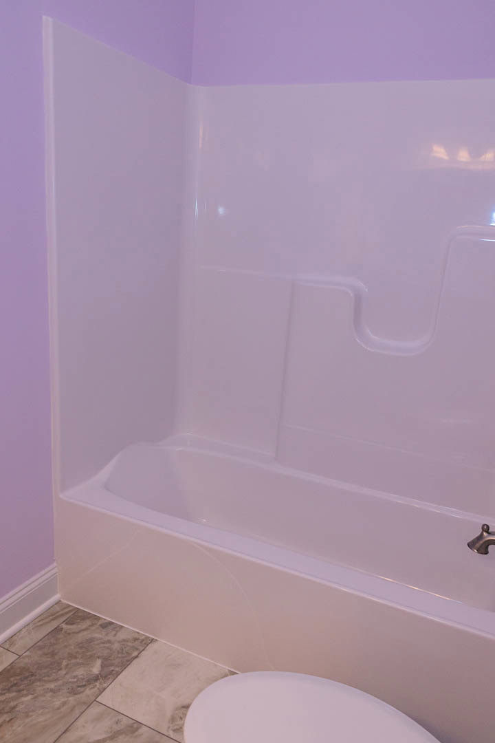 Freestanding white bathtub with chrome faucet set against marble tile floor and light-colored wall in modern bathroom
