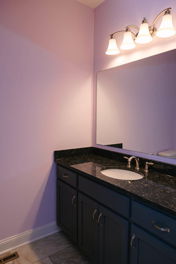 Marble countertop bathroom vanity with chrome faucet, rectangular sink, large framed mirror, brown floor vent on gray tile, and modern light fixture above