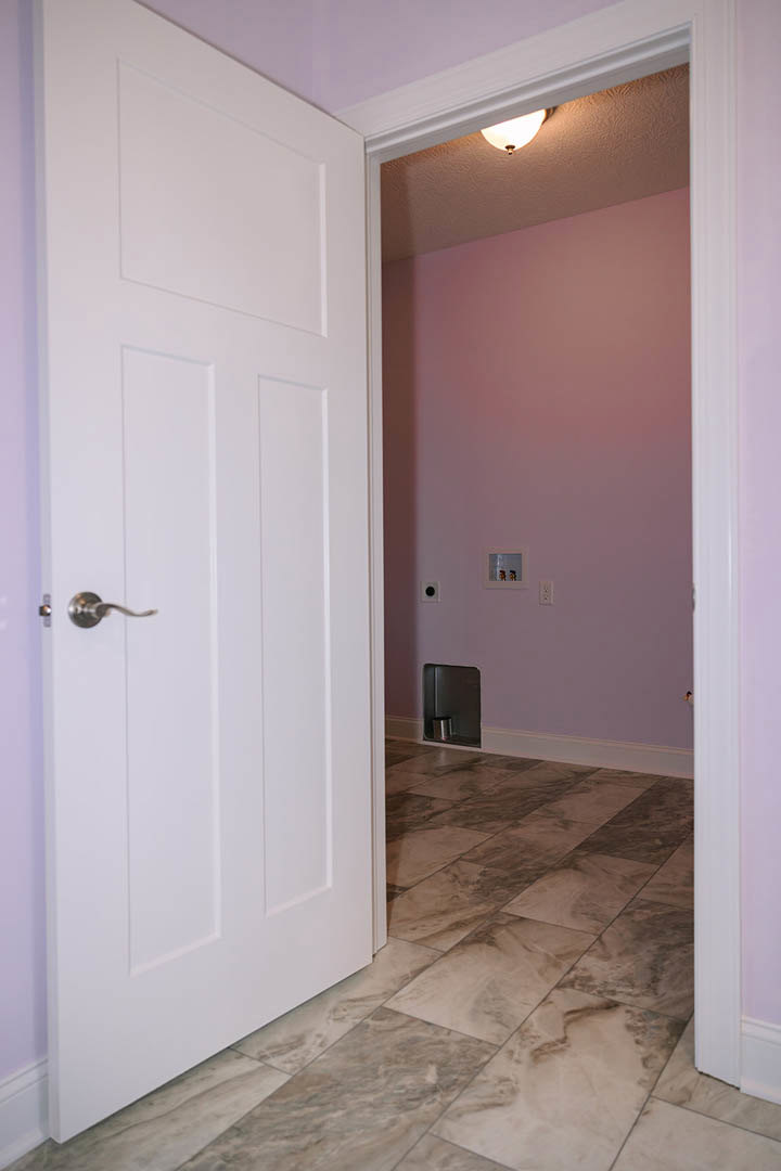 White door open to a room with a purple accent wall, metal container mounted on the wall, tile flooring, and ceiling light fixture visible