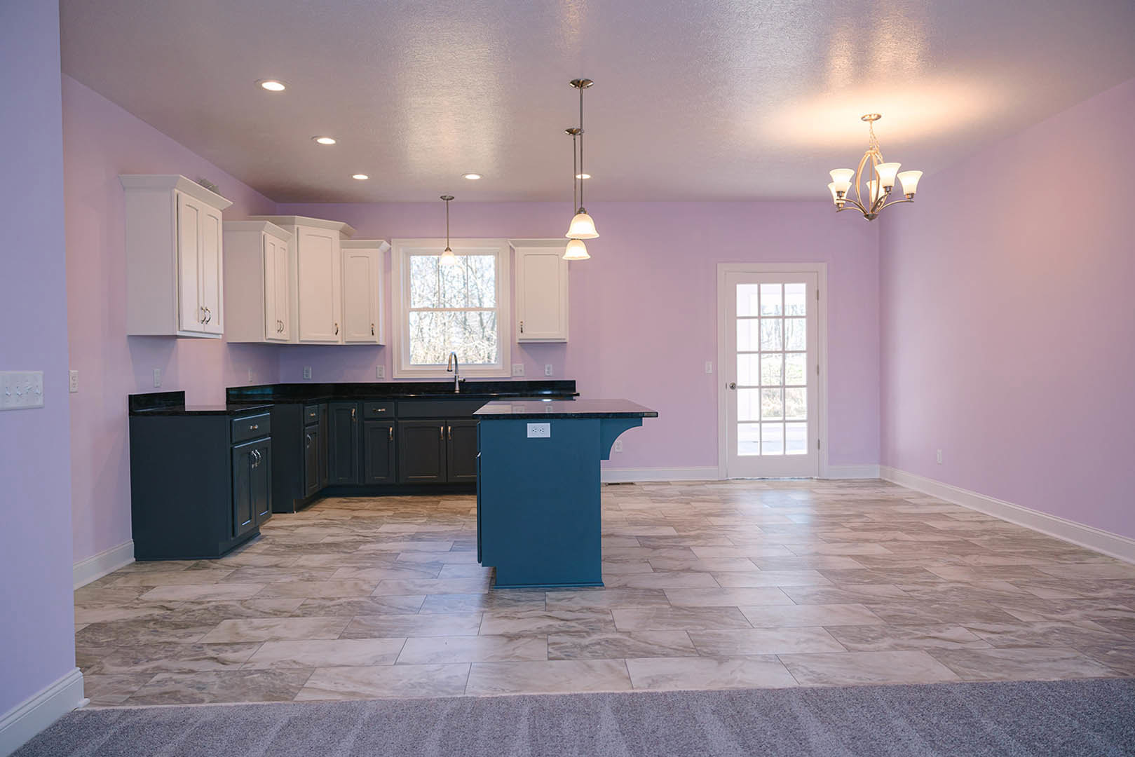 Purple-walled kitchen with matching purple countertop, blue island featuring black countertop, tile flooring with blue base, white door with glass panes, ceiling light, and window.