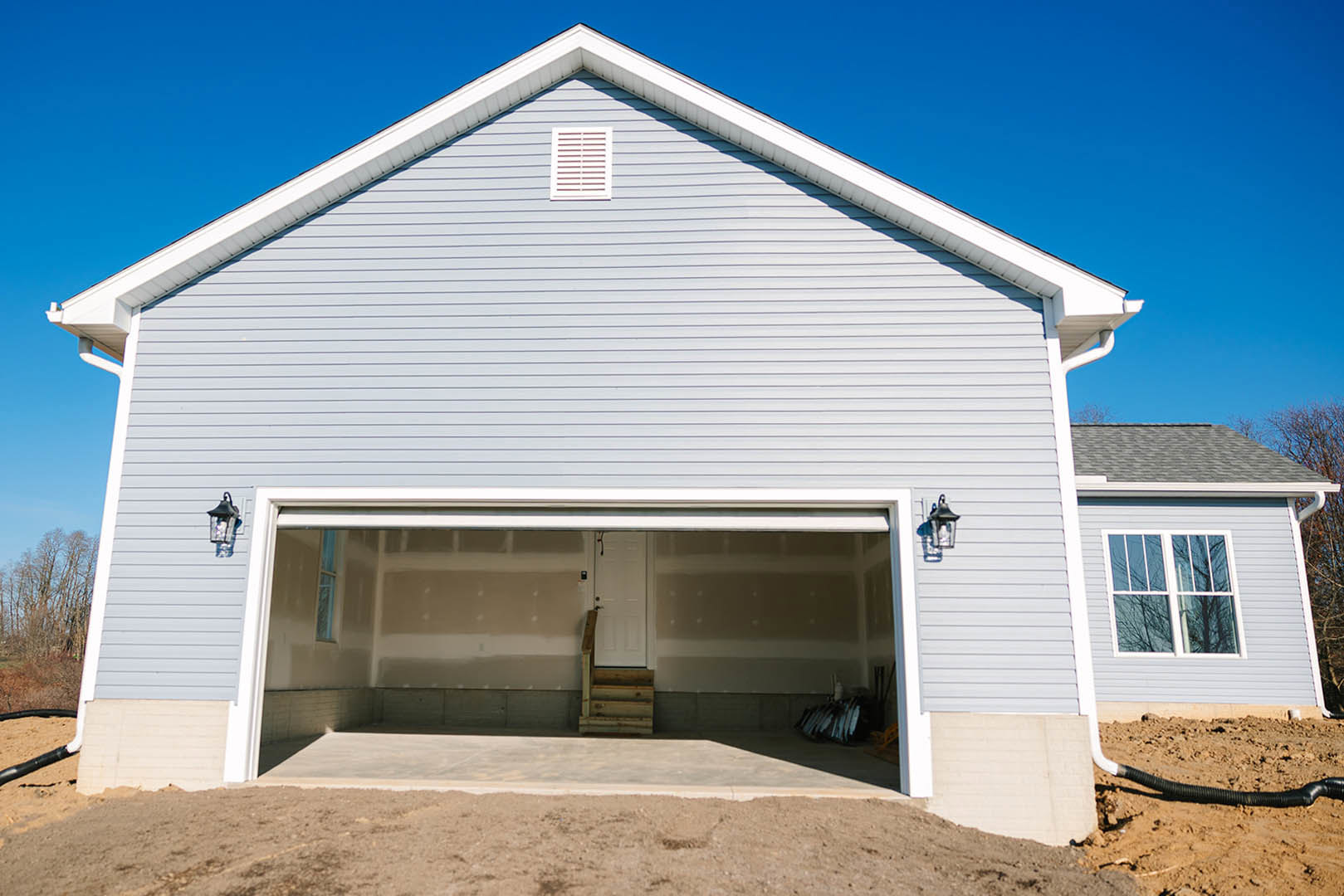 Detached garage with white siding, raised wooden staircase, open garage door, and adjacent window under clear sky