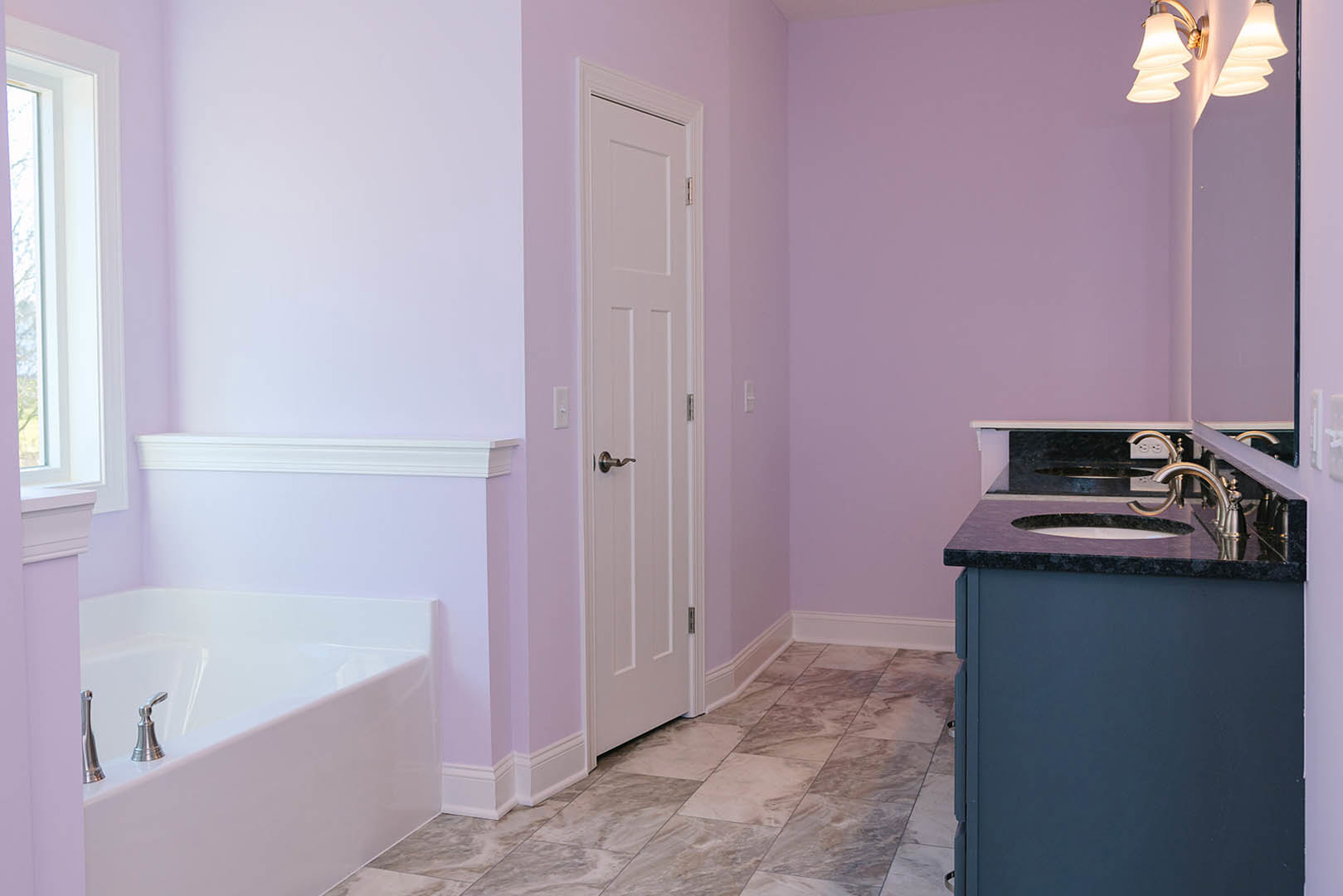 Modern bathroom featuring a freestanding bathtub with chrome faucets, white ceramic sink set in a wood vanity, tile flooring, and a white paneled door.